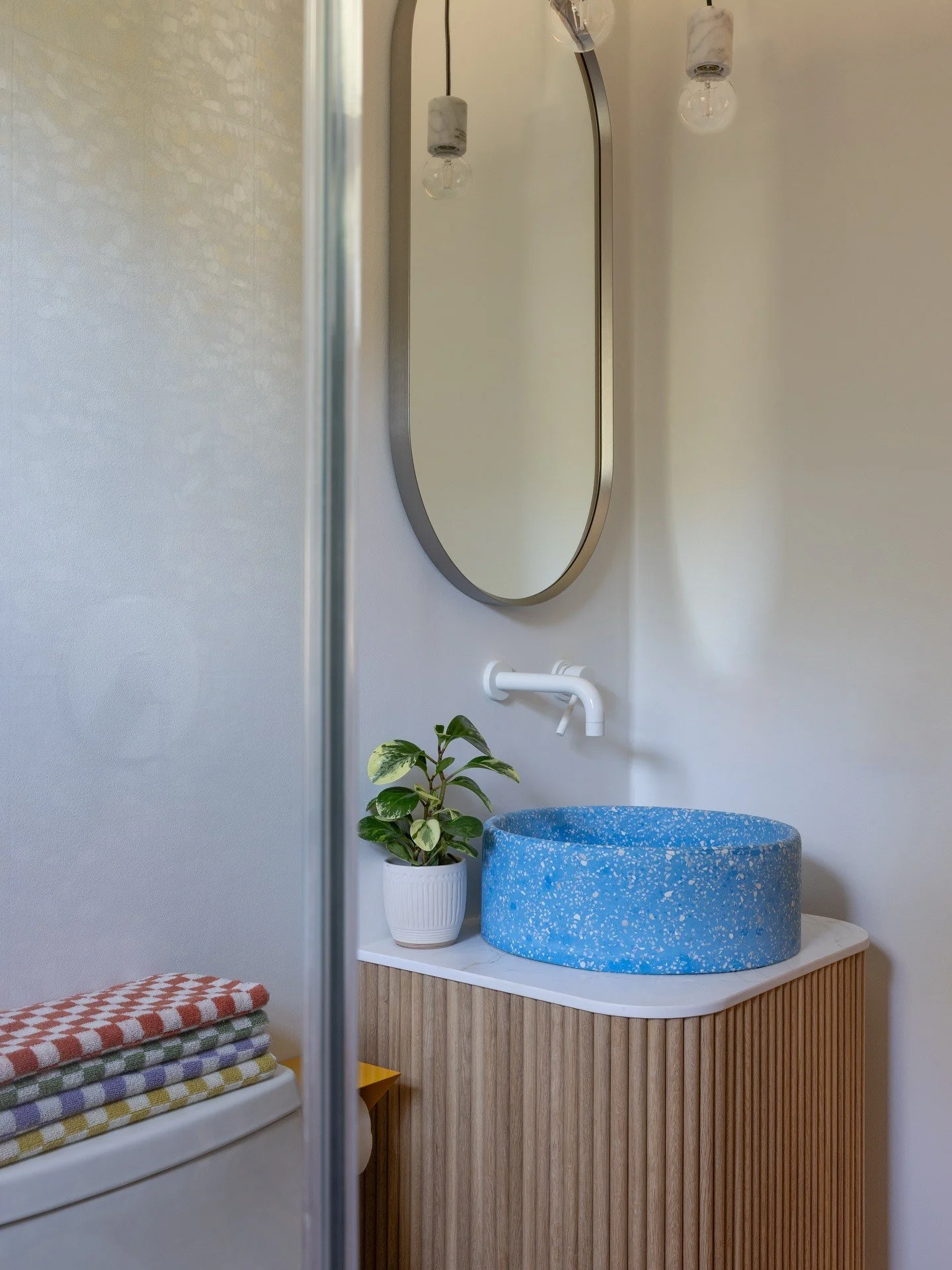 Round mirror above a blue basin and fluted wood cabinet