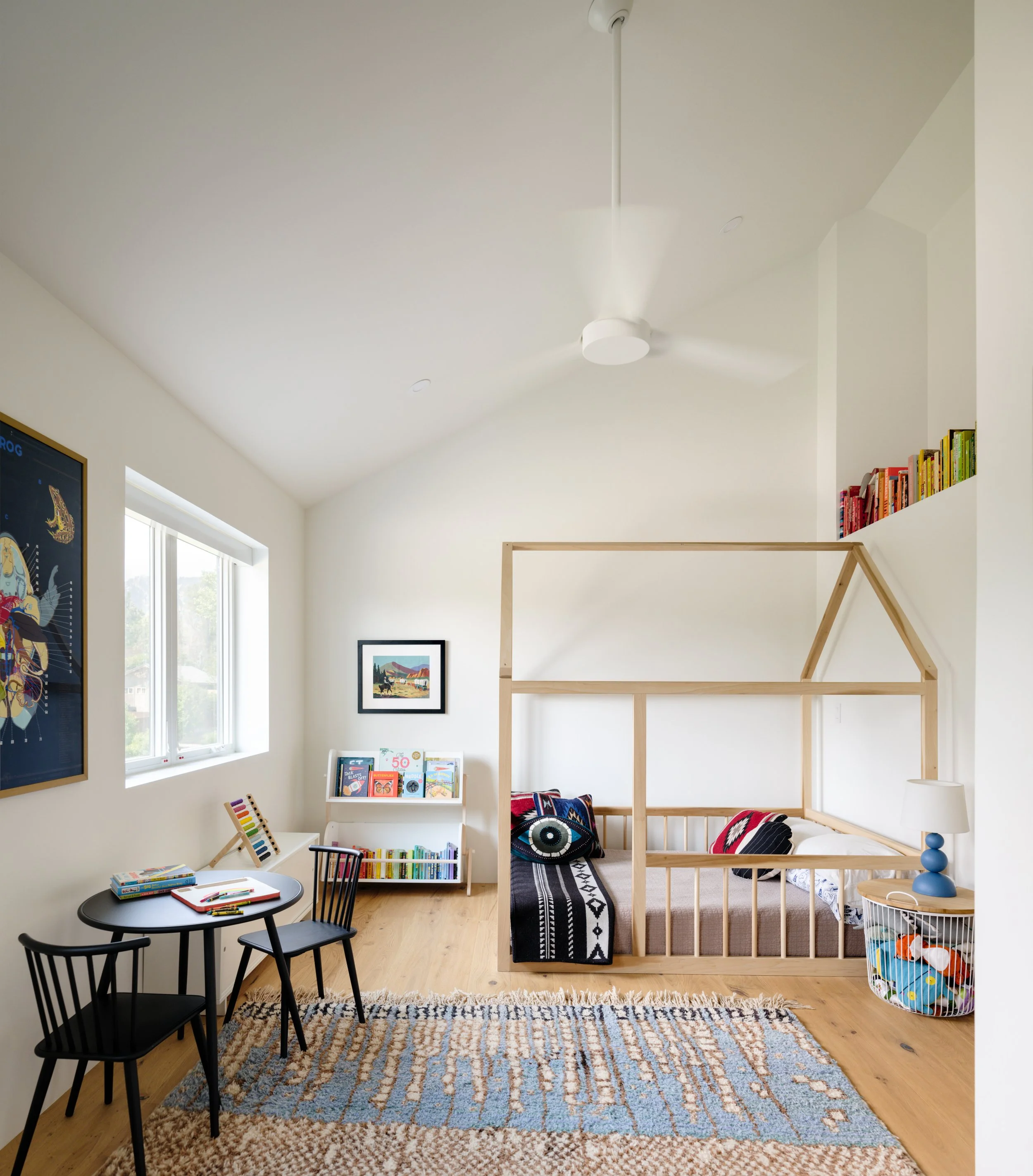 Bright child’s bedroom with a house-shaped bed frame, books, and a patterned rug.