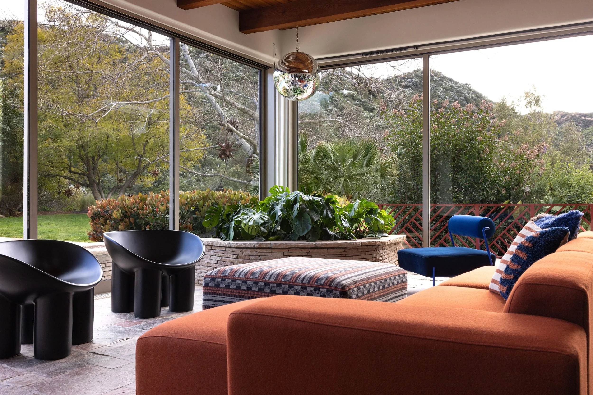 Glass-walled solarium with an orange sofa, sculptural black chairs and a view of the garden.