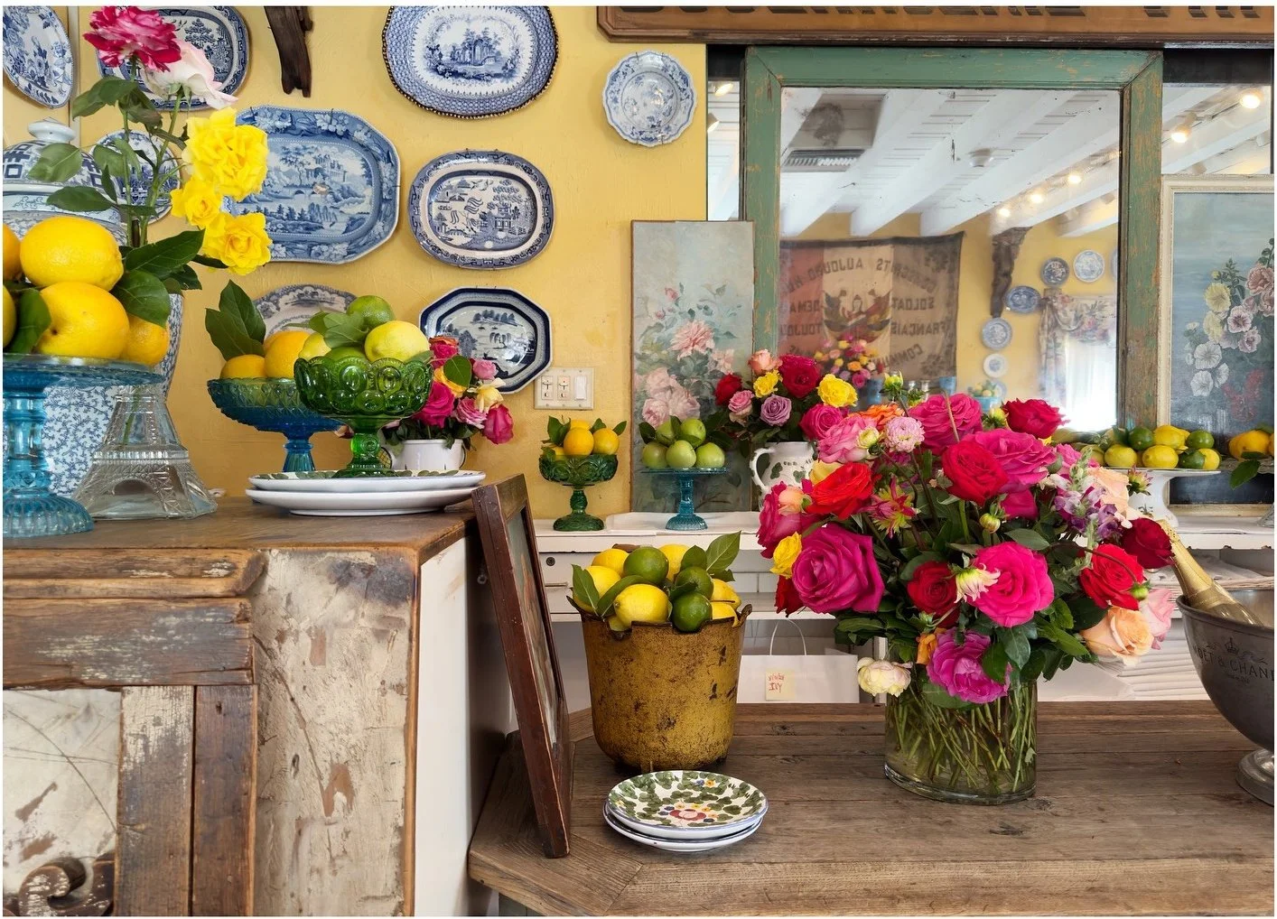 Flower arrangements and yellow lemons beneath a framed mirror