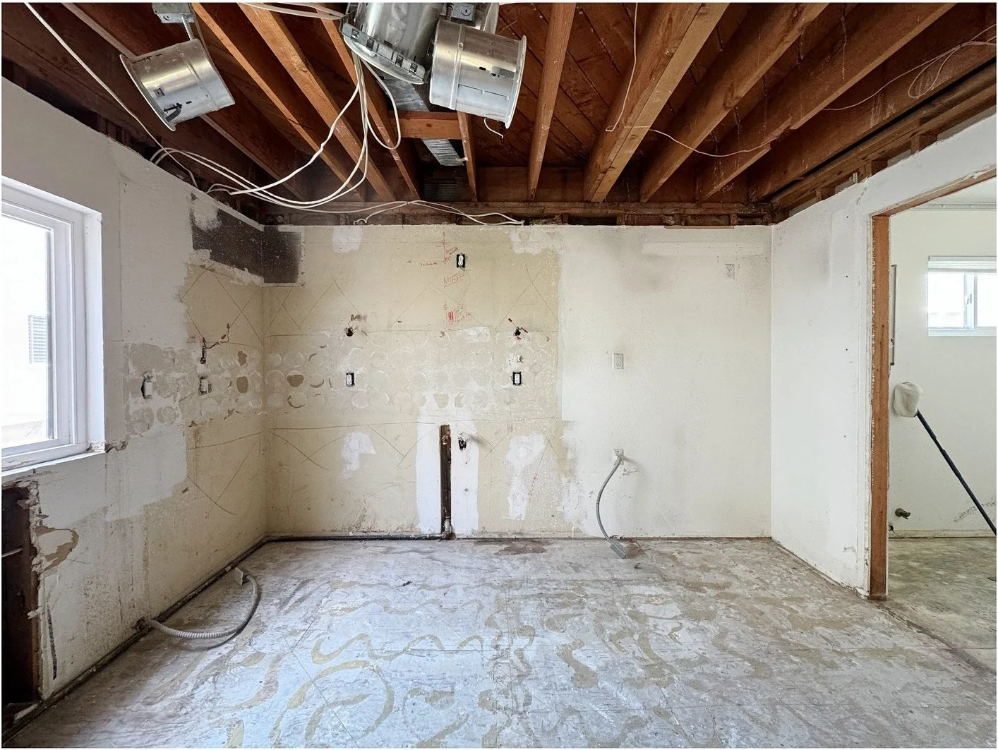 Stripped kitchen walls beneath exposed wood ceiling framing