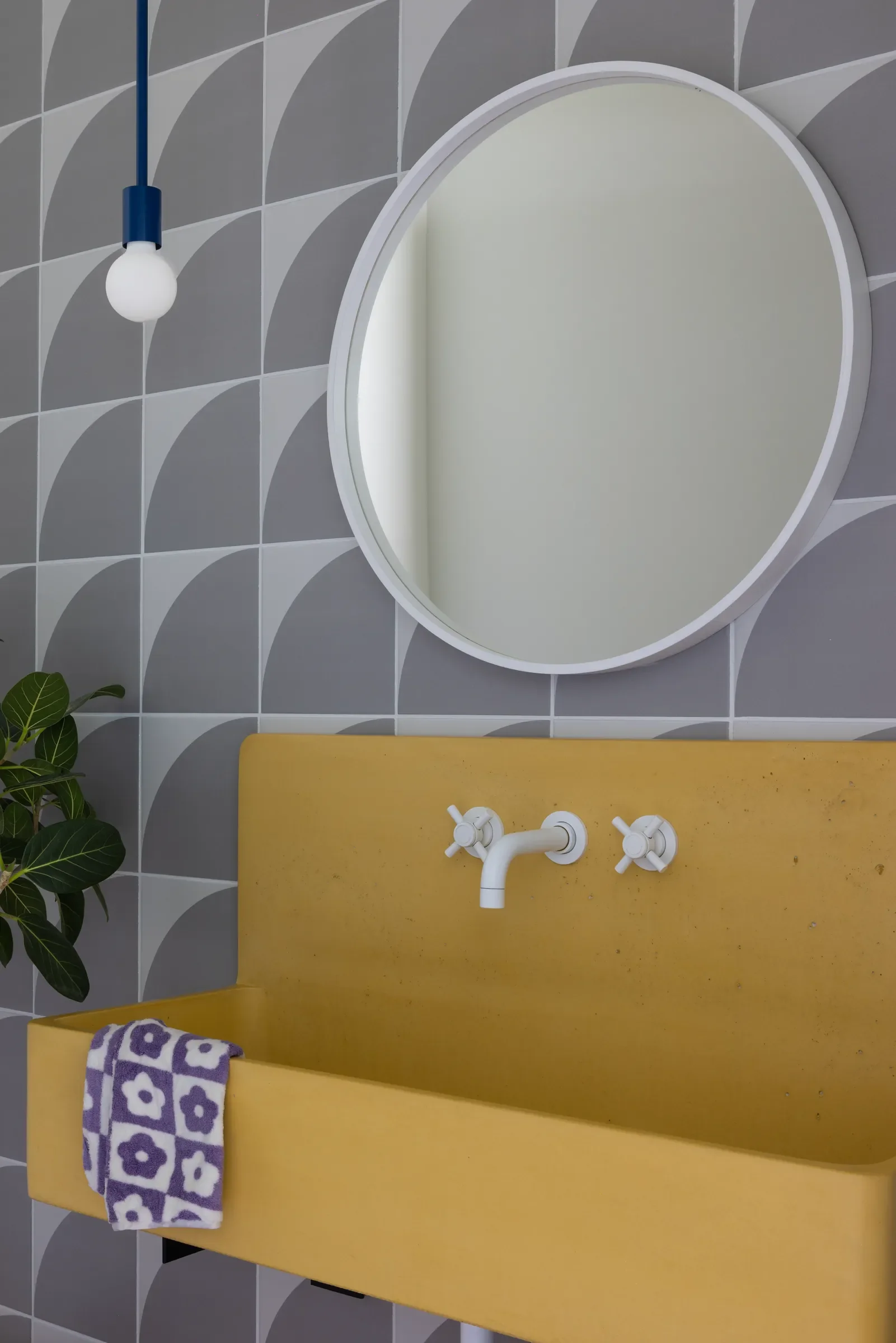 Yellow wall-mounted sink and round mirror against geometric gray tile.