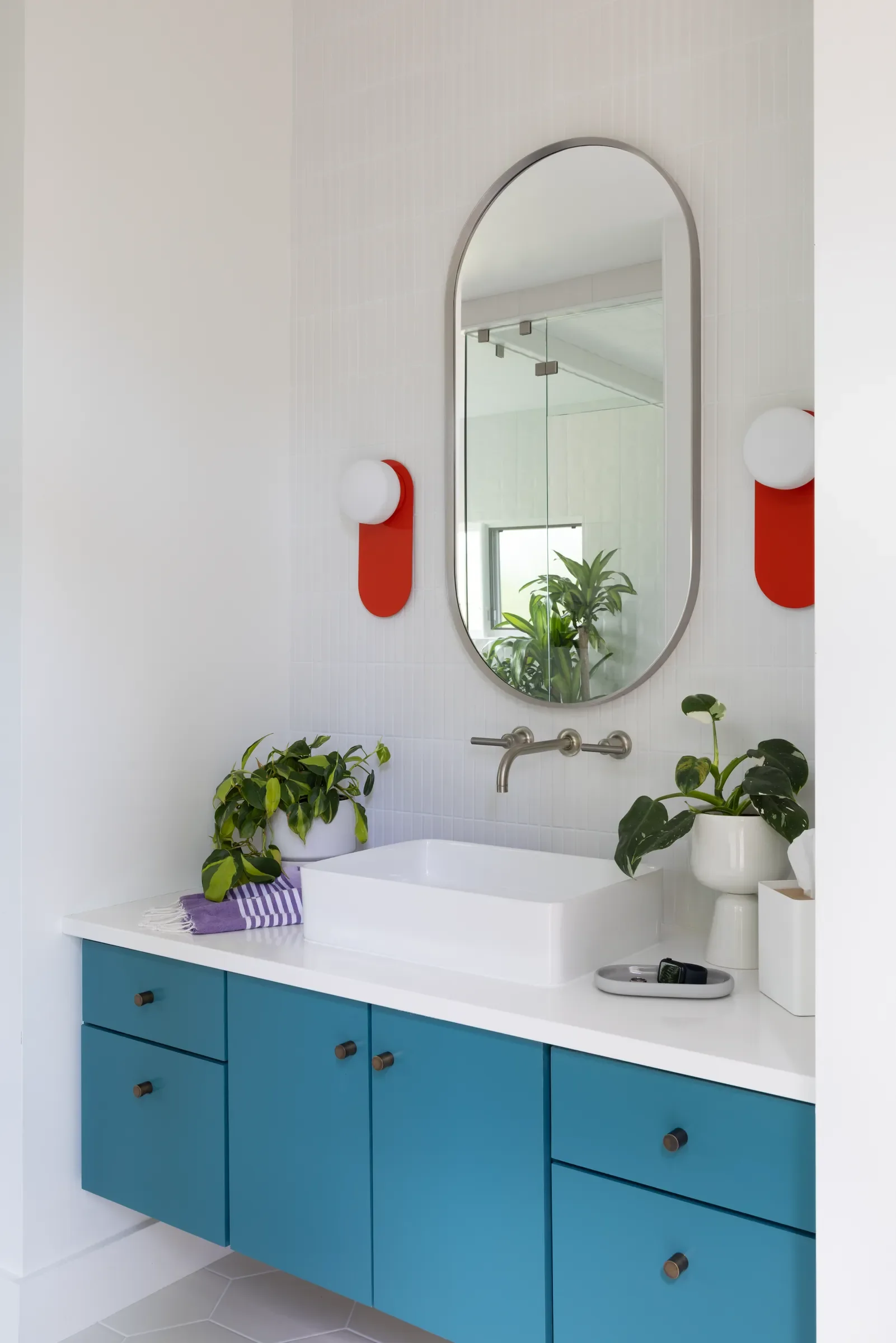 Blue bathroom vanity with an oval mirror and red wall sconces.