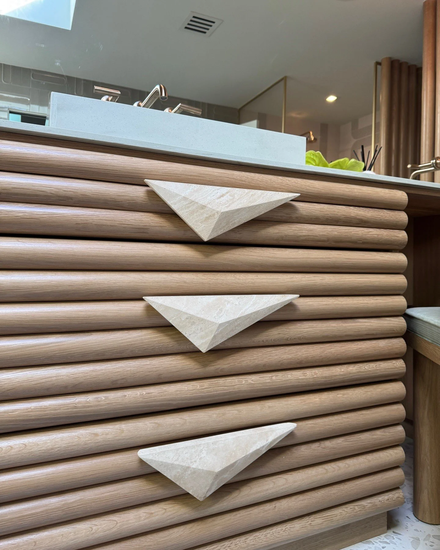 Close-up of a slatted wood vanity with triangular metal handles