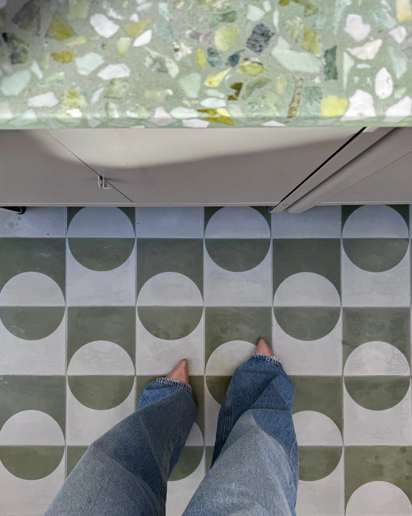 Pale green geometric tile floor beside a glass terrazzo table