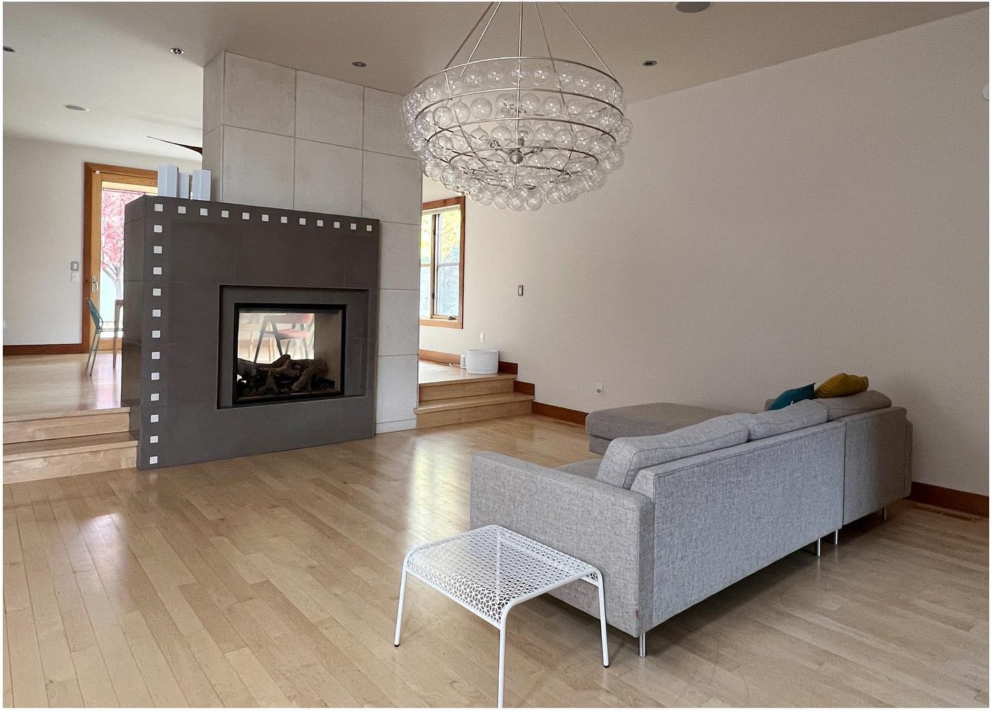 Original gray sofa and dark fireplace beneath a large chandelier