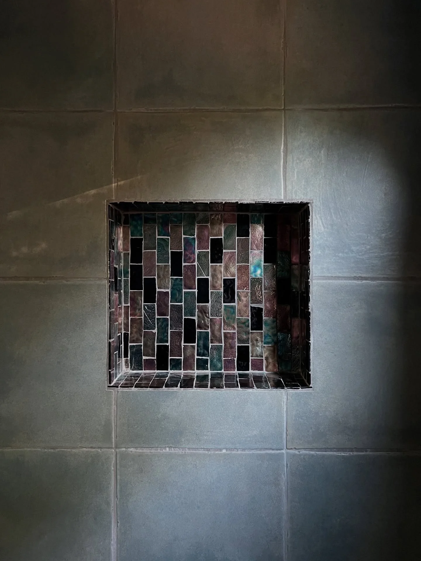 Dark tiled shower niche with multicolored mosaic inserts