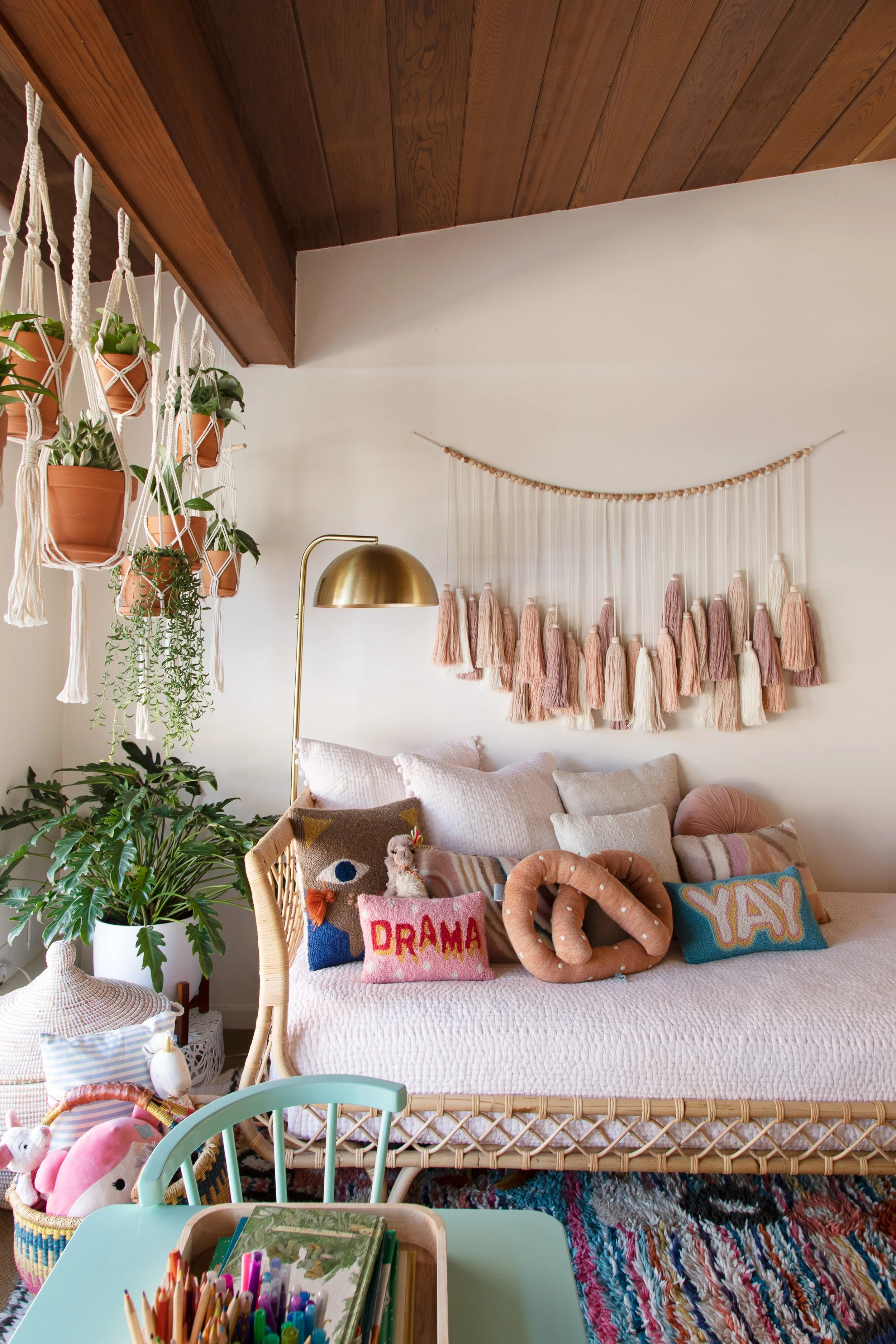 Child’s bedroom with a pink bed, tassel wall hanging, and plants.