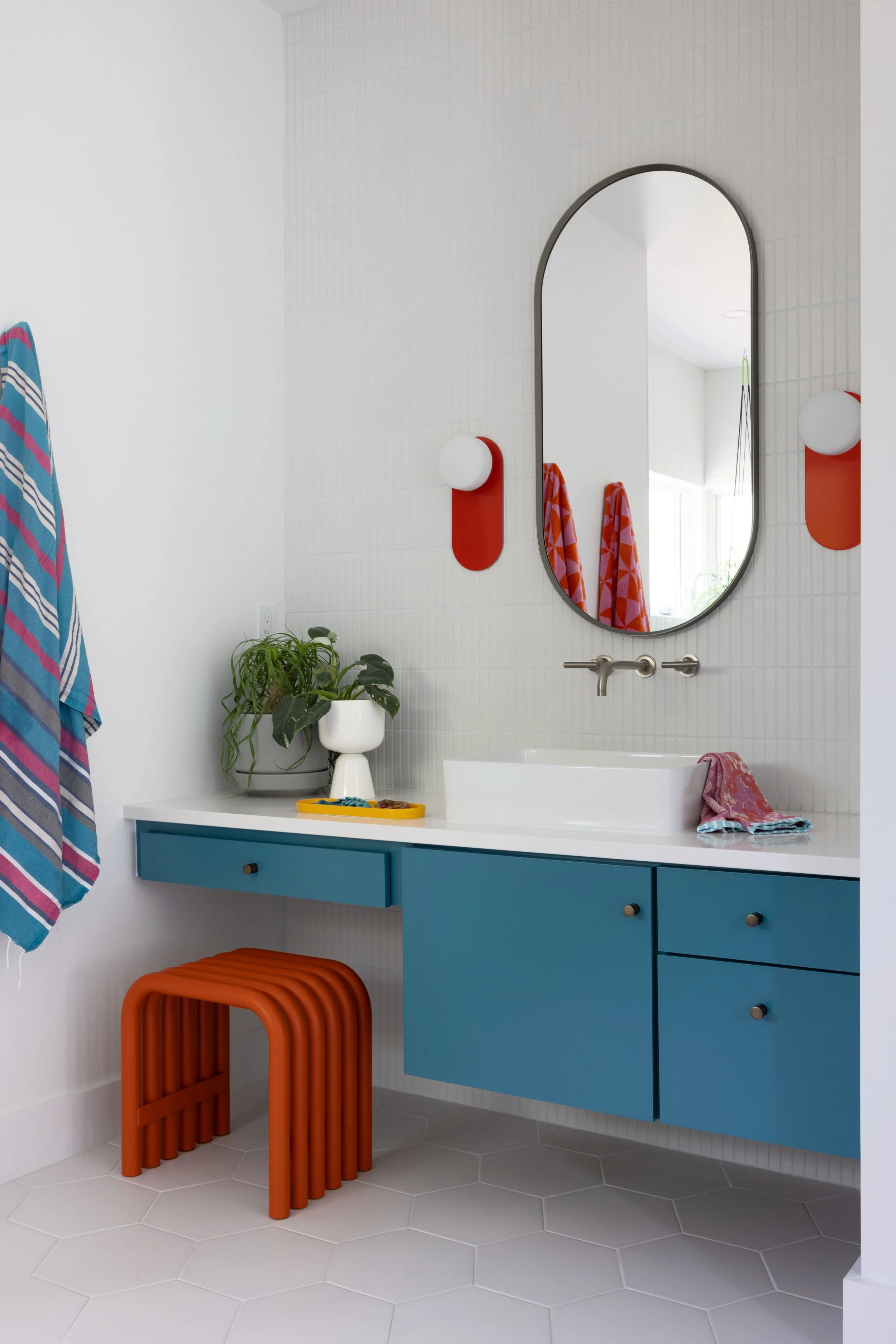 Bathroom with a blue floating vanity, oval mirror, and orange stool.