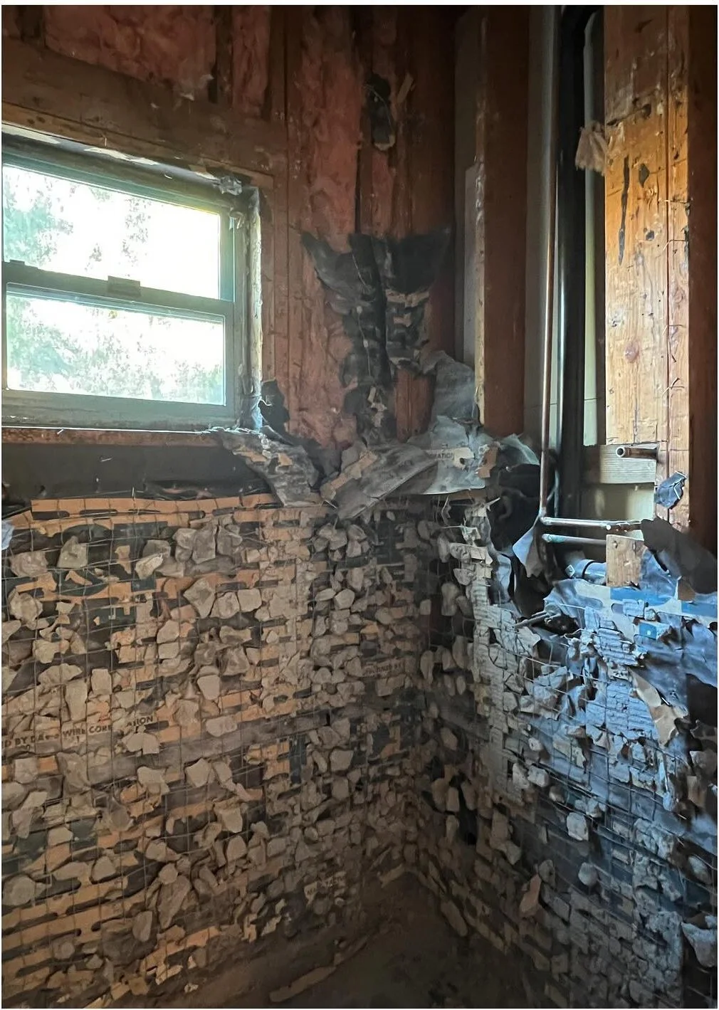 Bathroom demolition exposing rough wall surfaces around a window