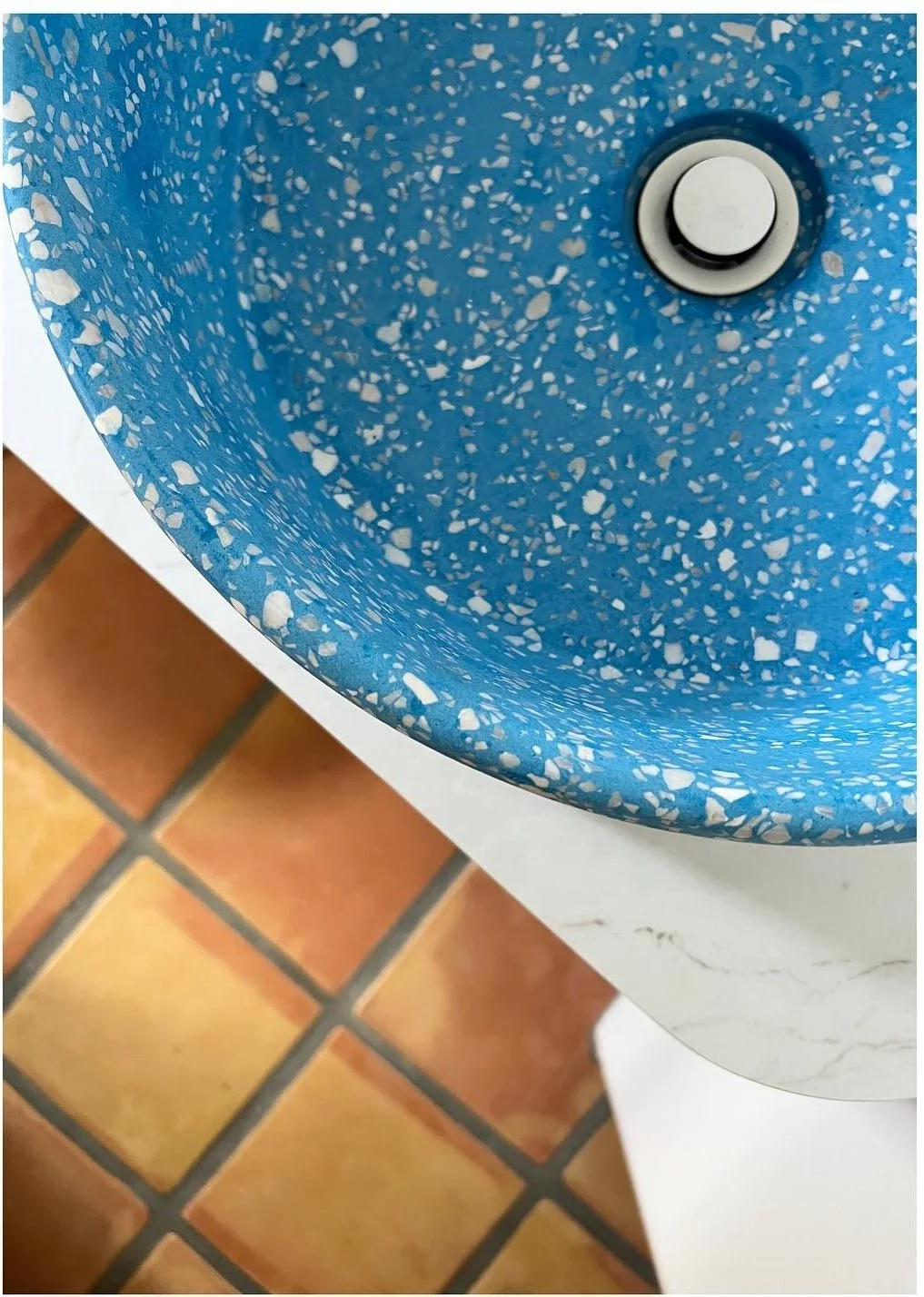 Overhead detail of a blue terrazzo basin above terracotta flooring