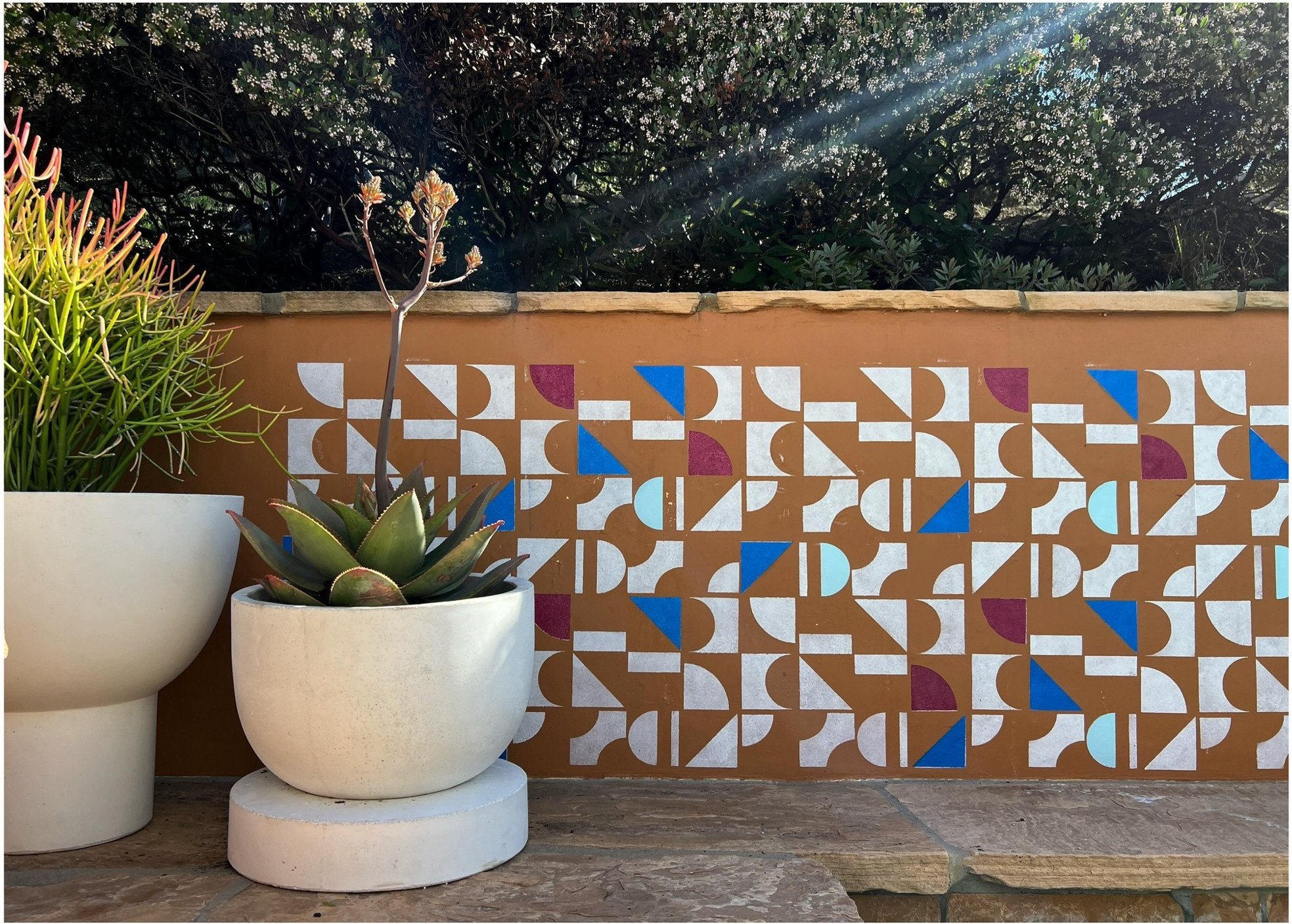 Pale sculptural plant pots beside a blue ochre and white geometric tile wall