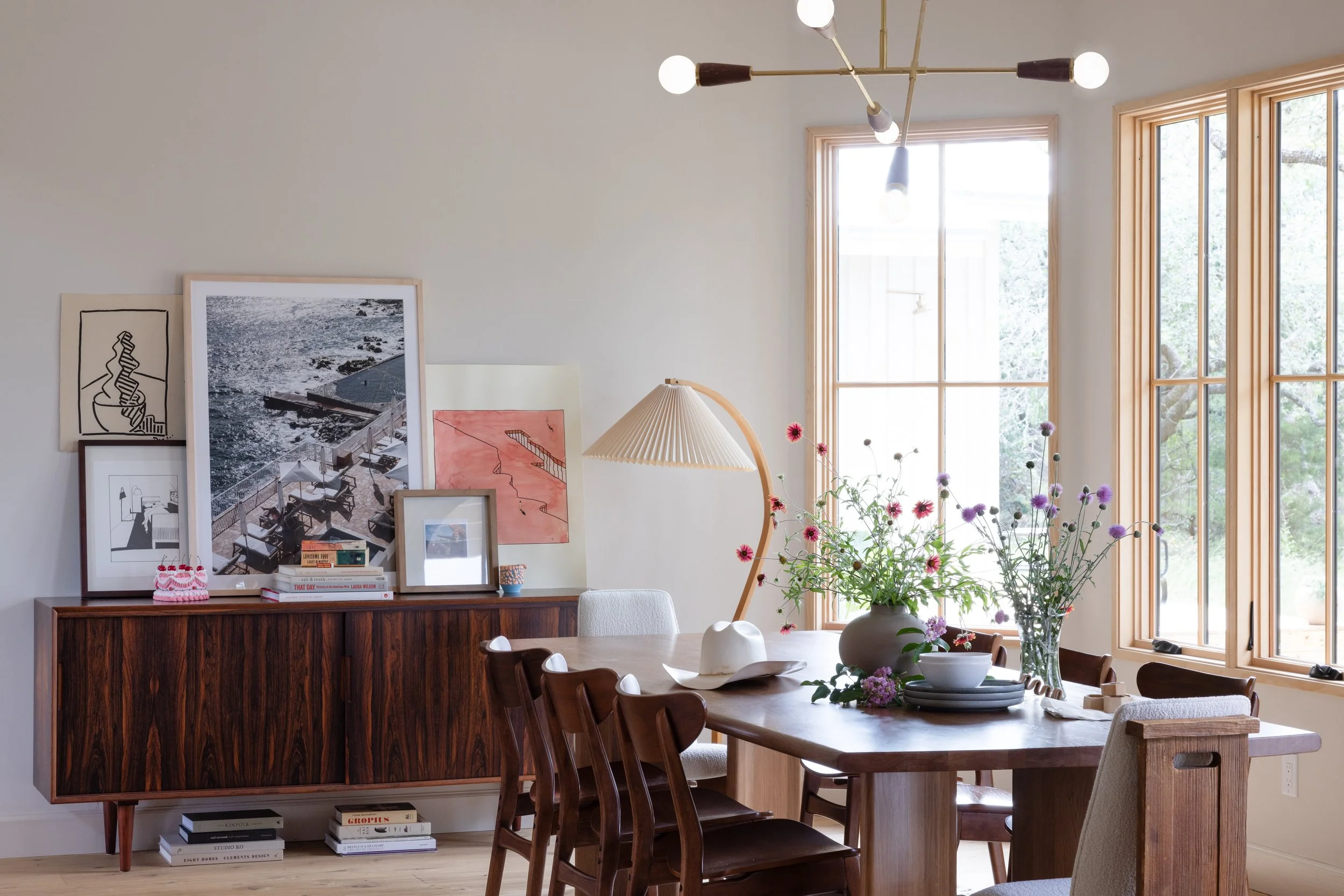 Dining room with a wood table, tall windows, and art displayed on a sideboard.