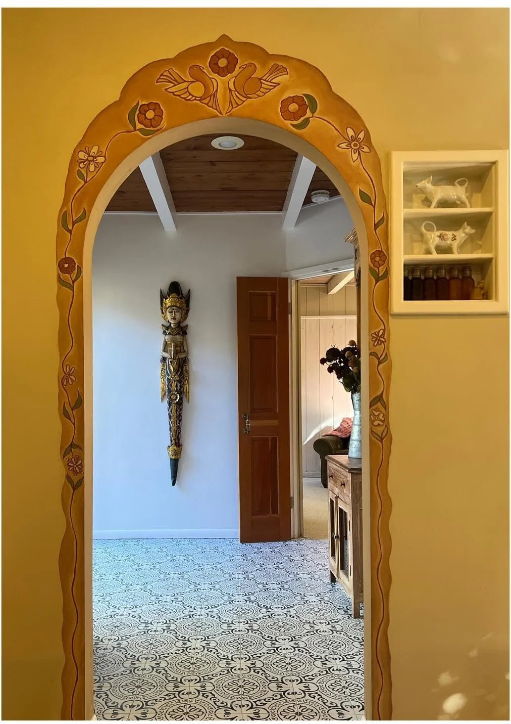 Ornate painted mirror frame on a mustard wall beside a tiled doorway