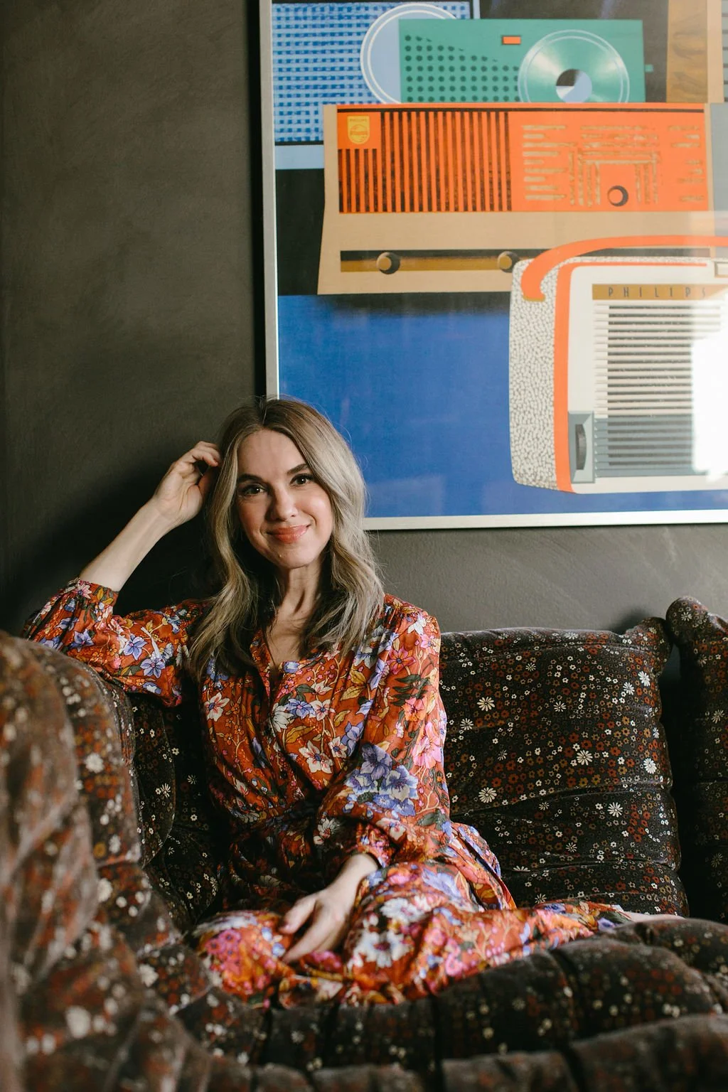 Amy Pigliacampo in a floral dress seated on a patterned sofa.