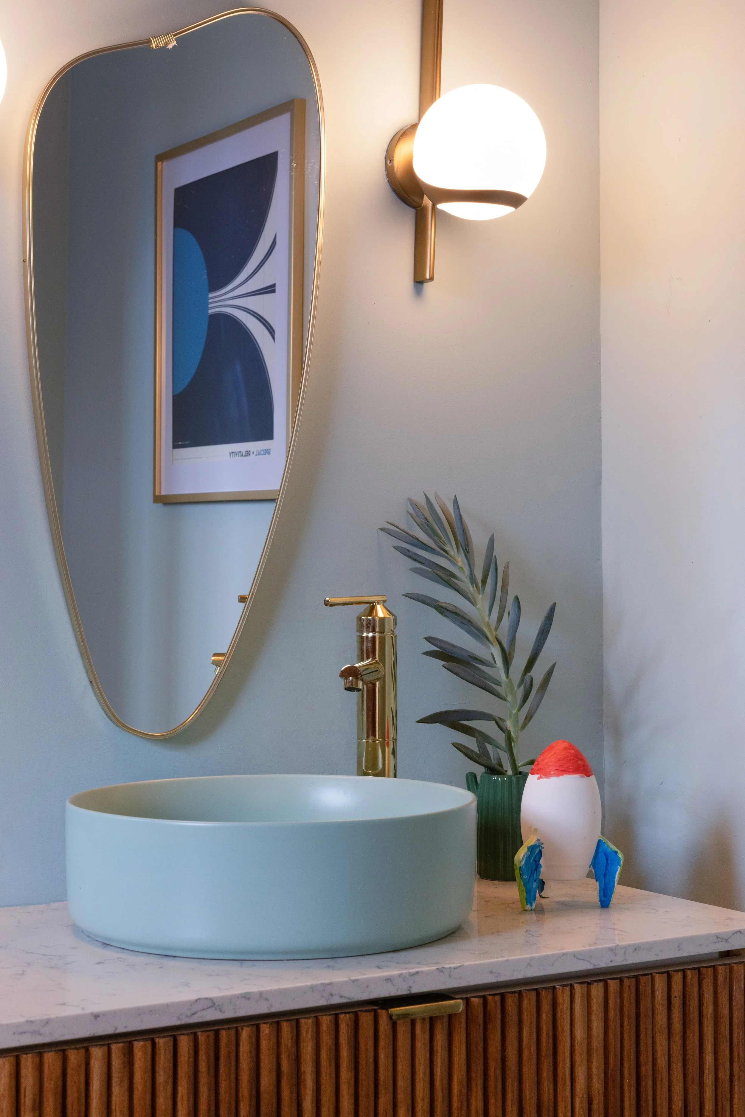 Bathroom with a blue vessel sink, brass faucet, oval mirror, and globe sconce.