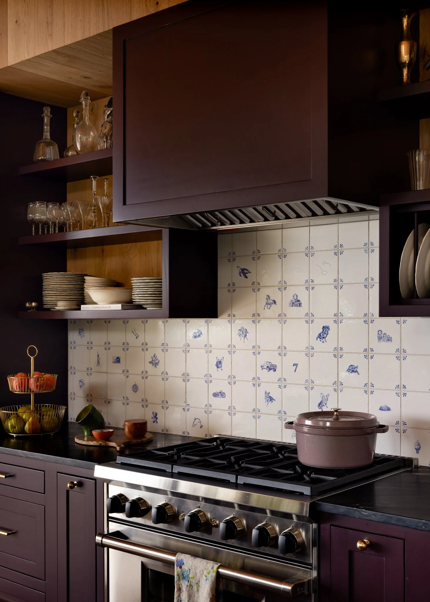 Plum kitchen cabinetry and a stainless range framed by blue-and-white patterned tile.
