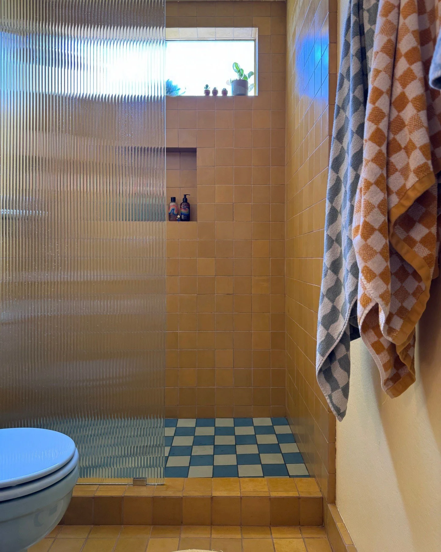 Yellow tiled shower with checkerboard floor and patterned curtain