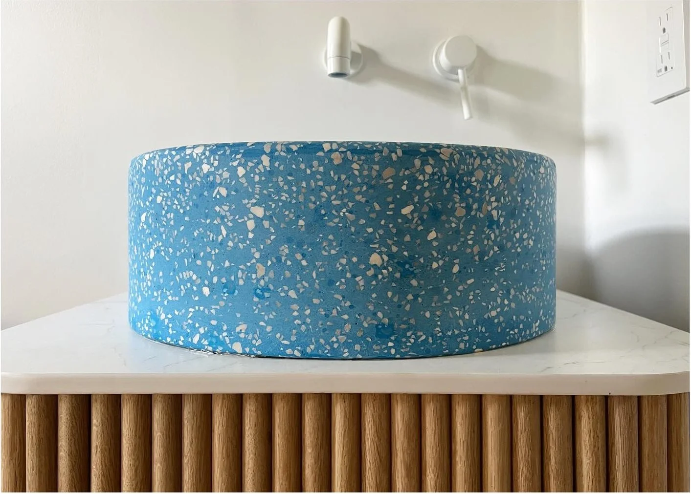 Blue basin and white wall faucet above a fluted oak vanity