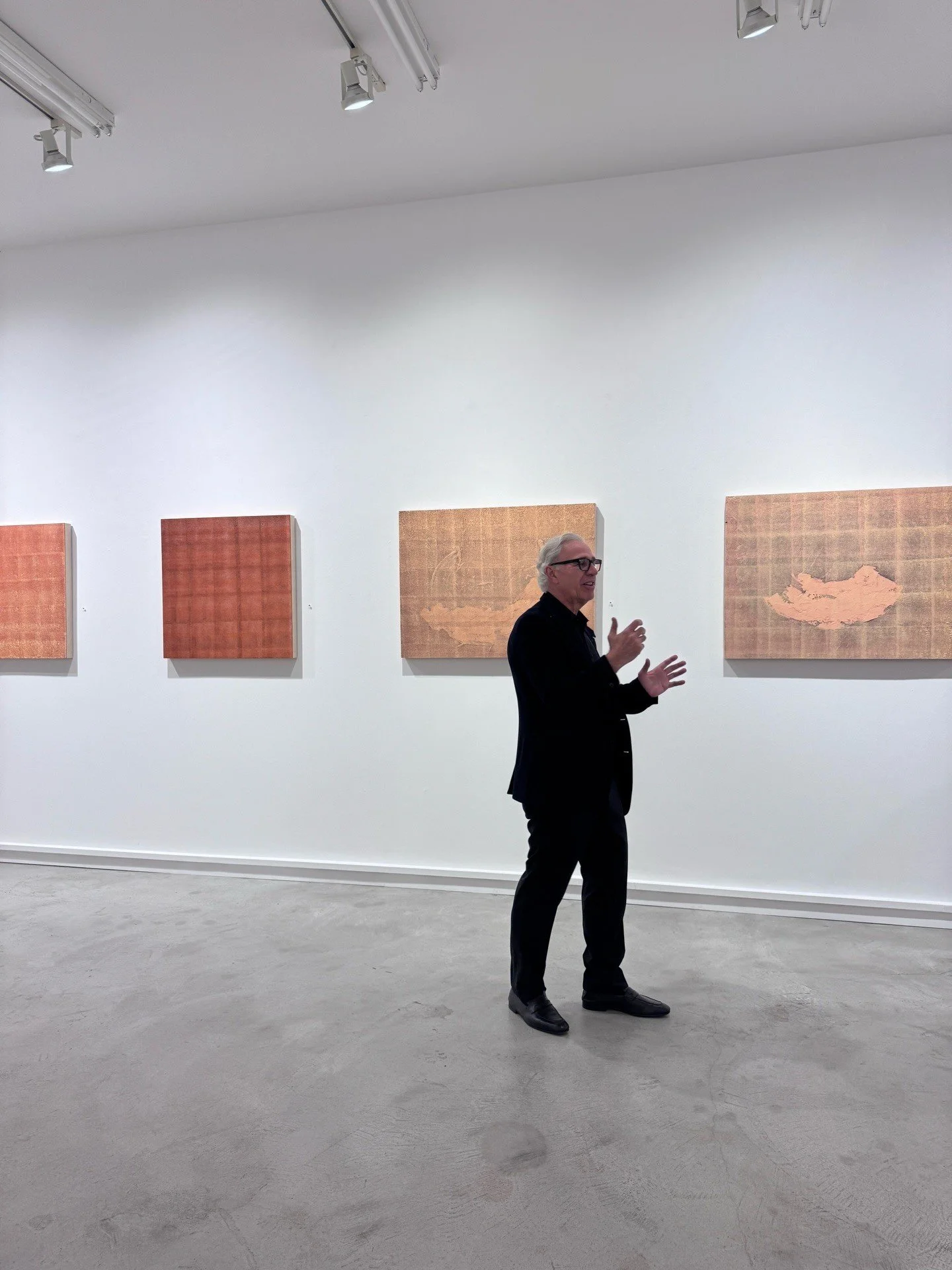 Artist speaking beside square paintings in a white gallery