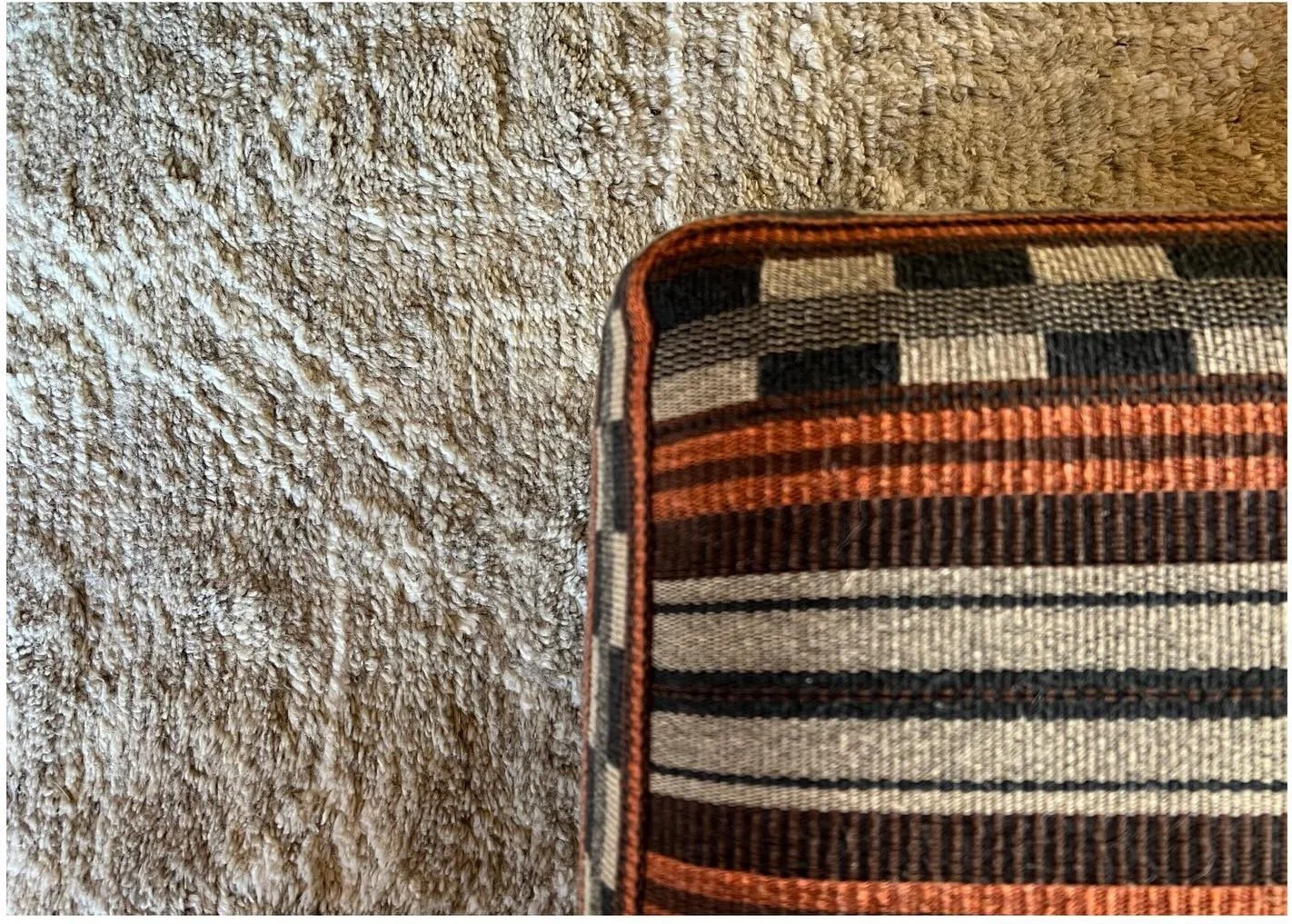 Corner of a striped upholstered ottoman on a textured pale rug