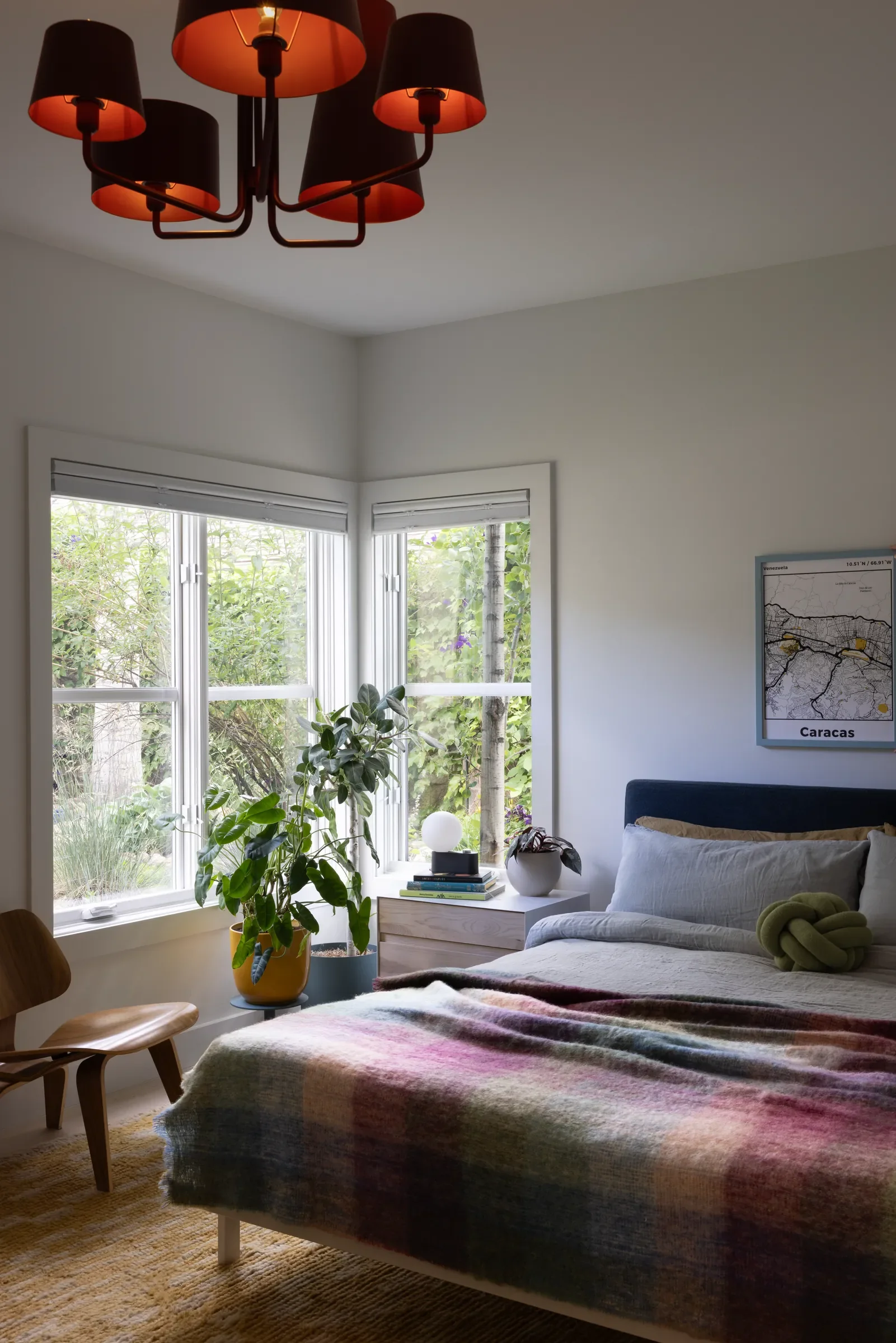 Bedroom with a plaid blanket, plants by the windows, and a red ceiling light.