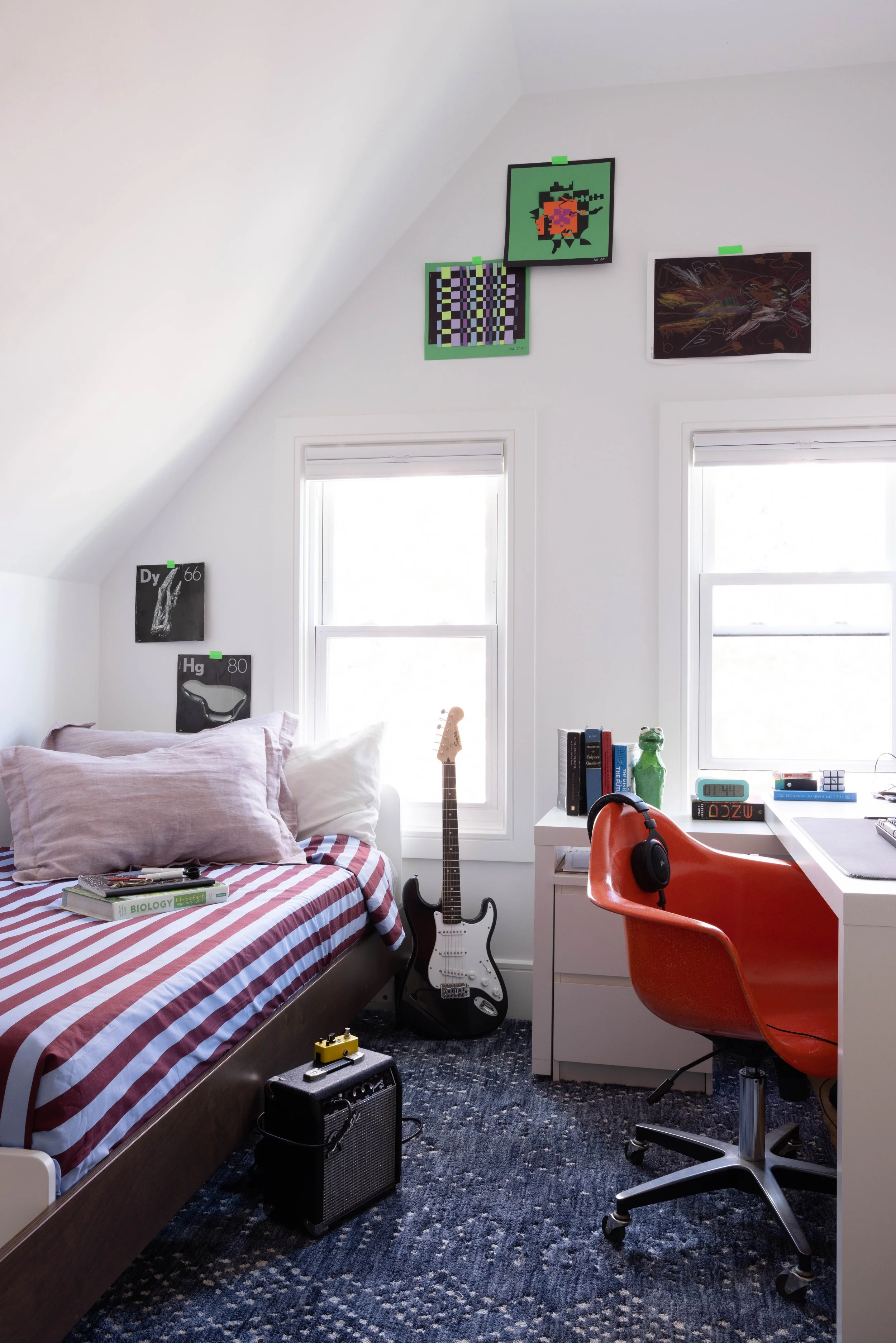 Bedroom with a striped bed, guitars, red desk chair, and sloped ceiling.