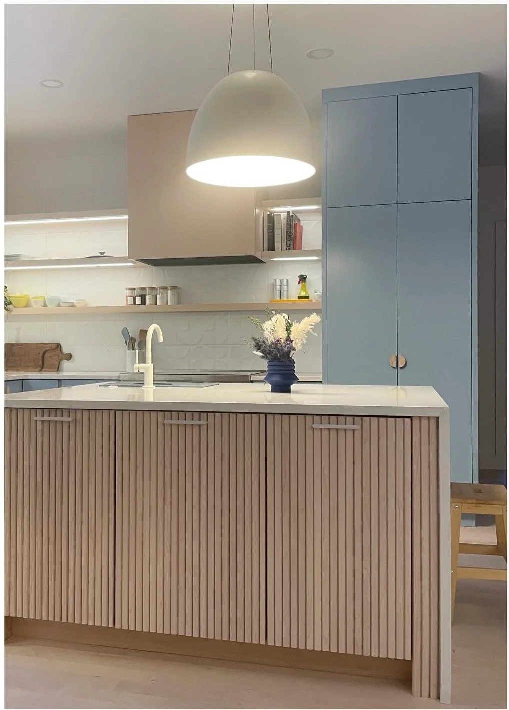Fluted wood kitchen peninsula beneath a pale pendant light