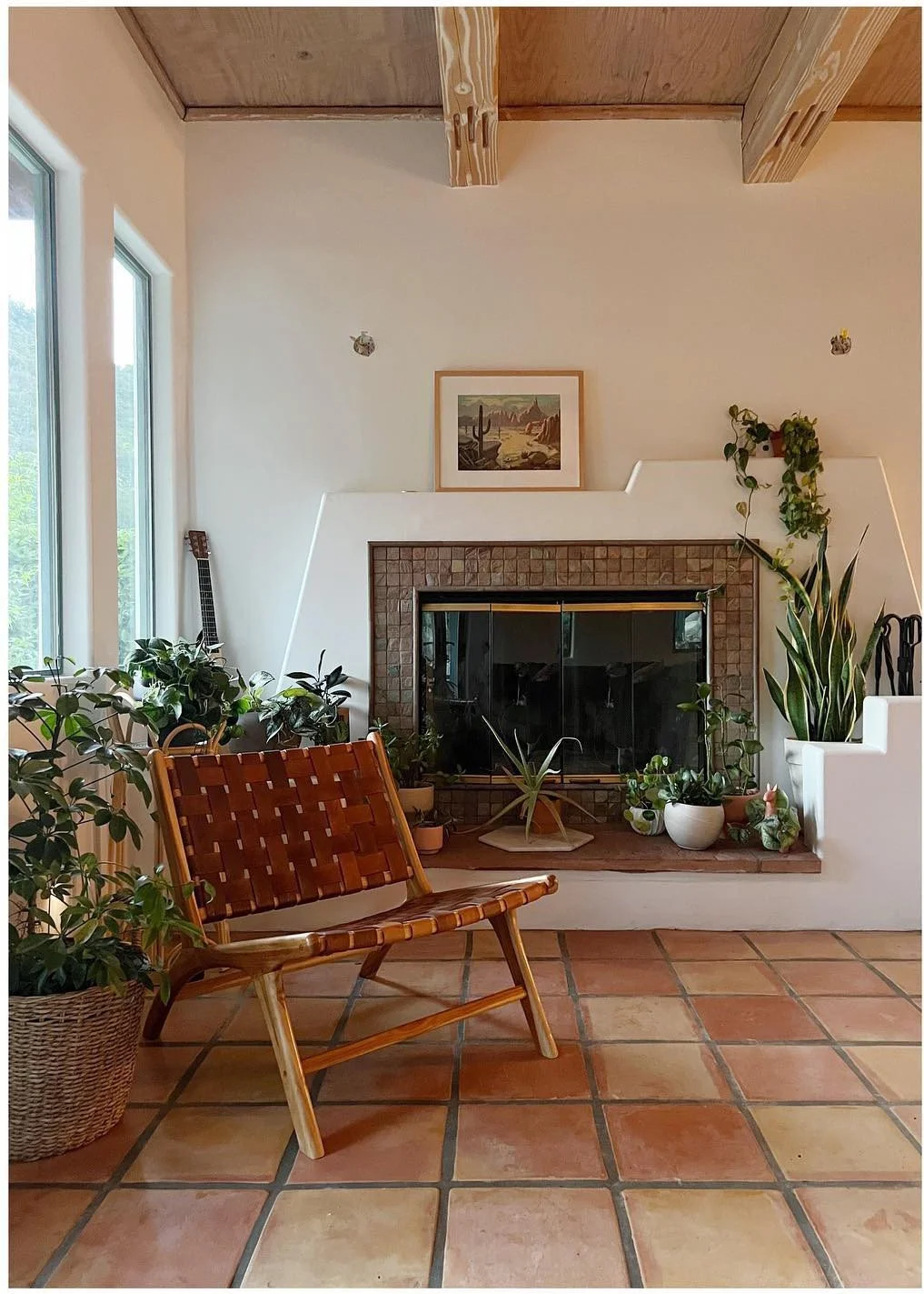 Wood-framed lounge chair beside a fireplace plants and terracotta floor tiles