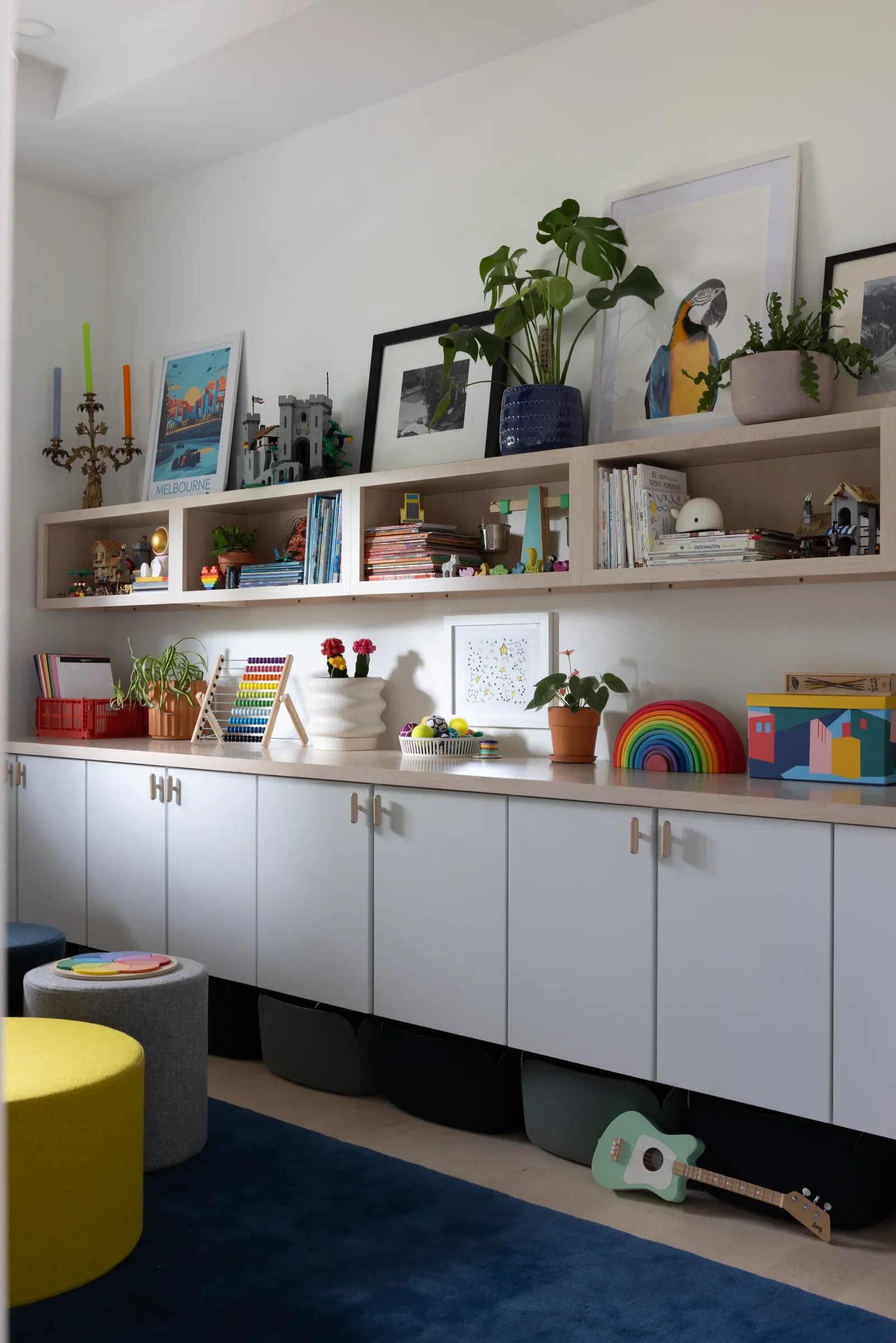 Playroom shelving with books, toys, artwork, and white cabinets.