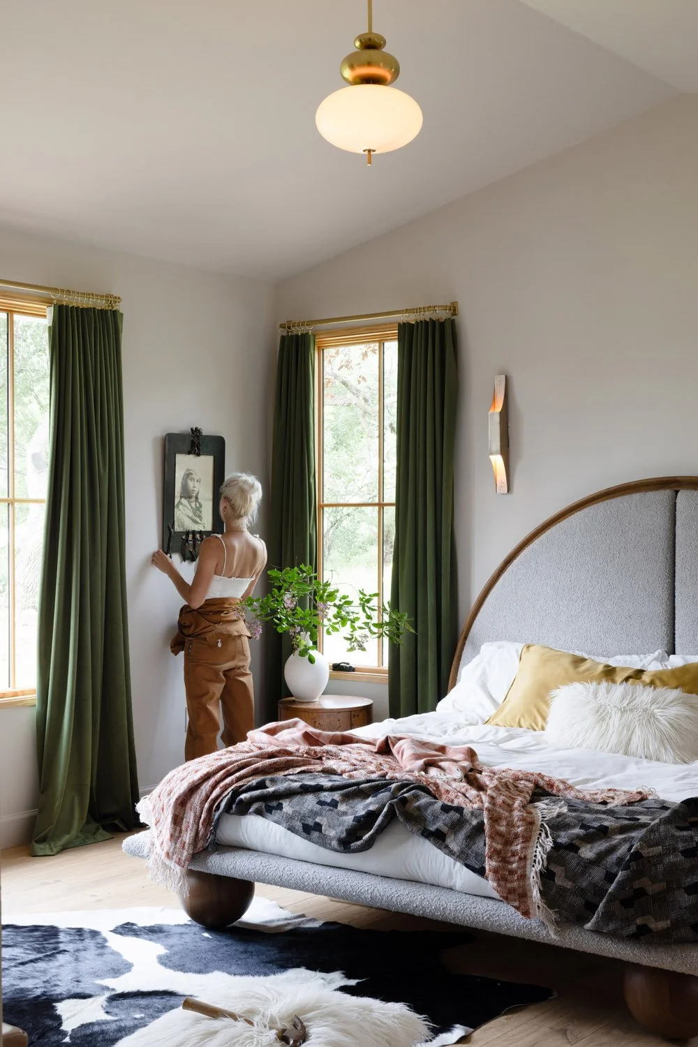 Bedroom with green curtains, upholstered bed, and a person standing by the window.