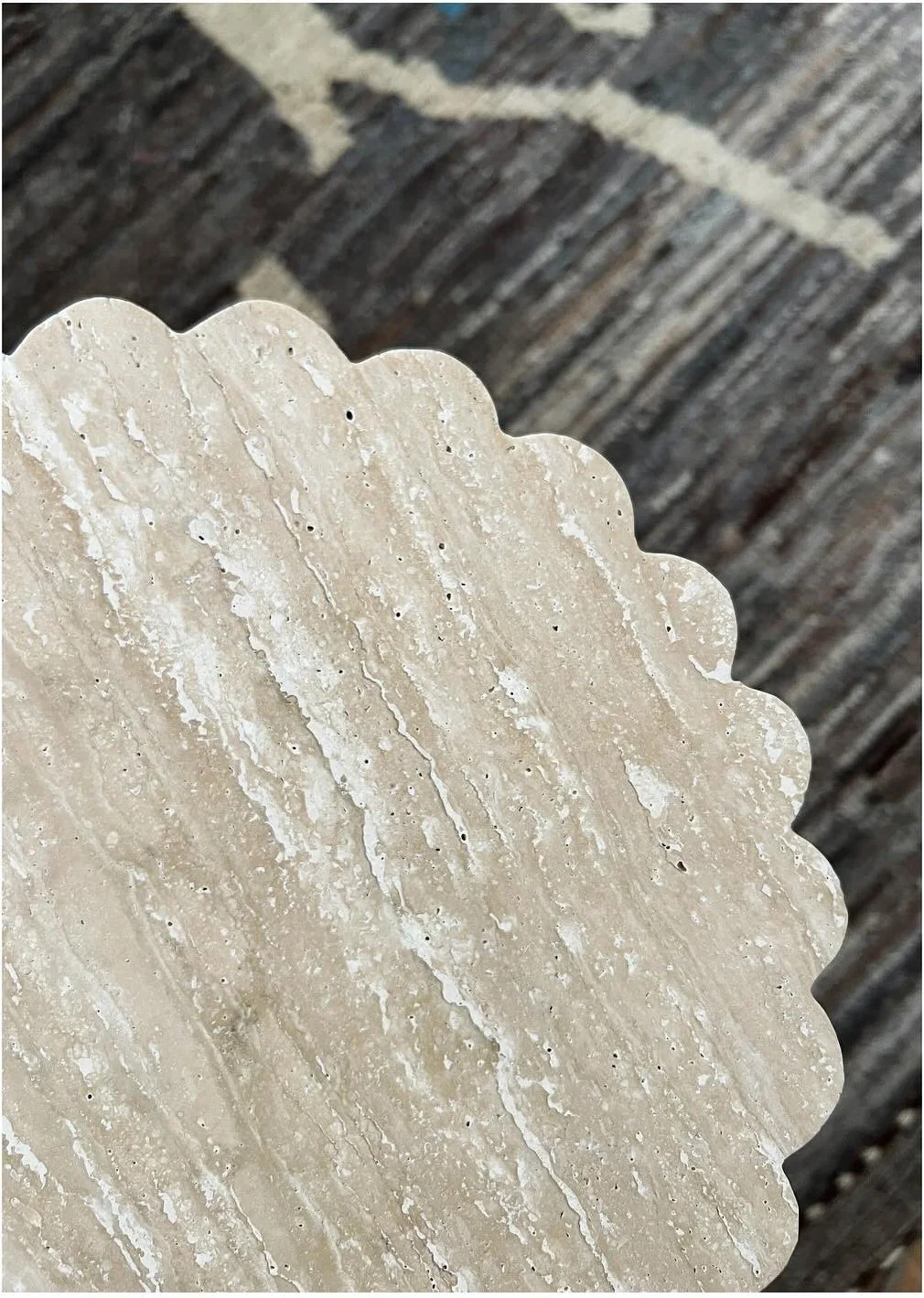 Close-up of a scalloped pale stone tabletop on a dark rug