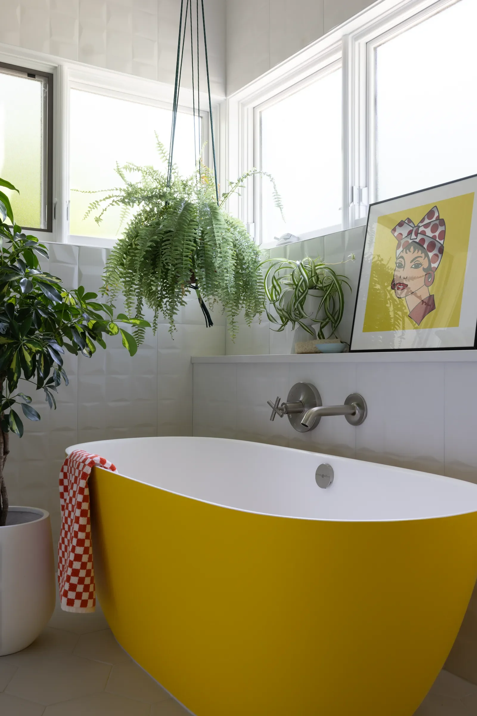 Yellow freestanding bathtub beneath a window, surrounded by plants.