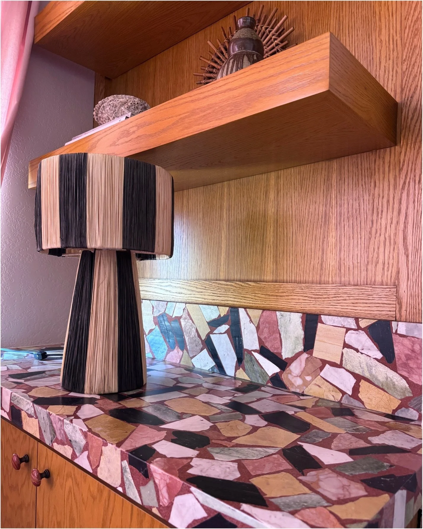 Wood shelves and a lamp above a multicolored stone counter