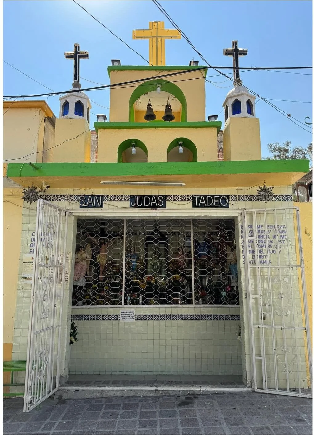 Green and yellow chapel facade with crosses above a metal gate