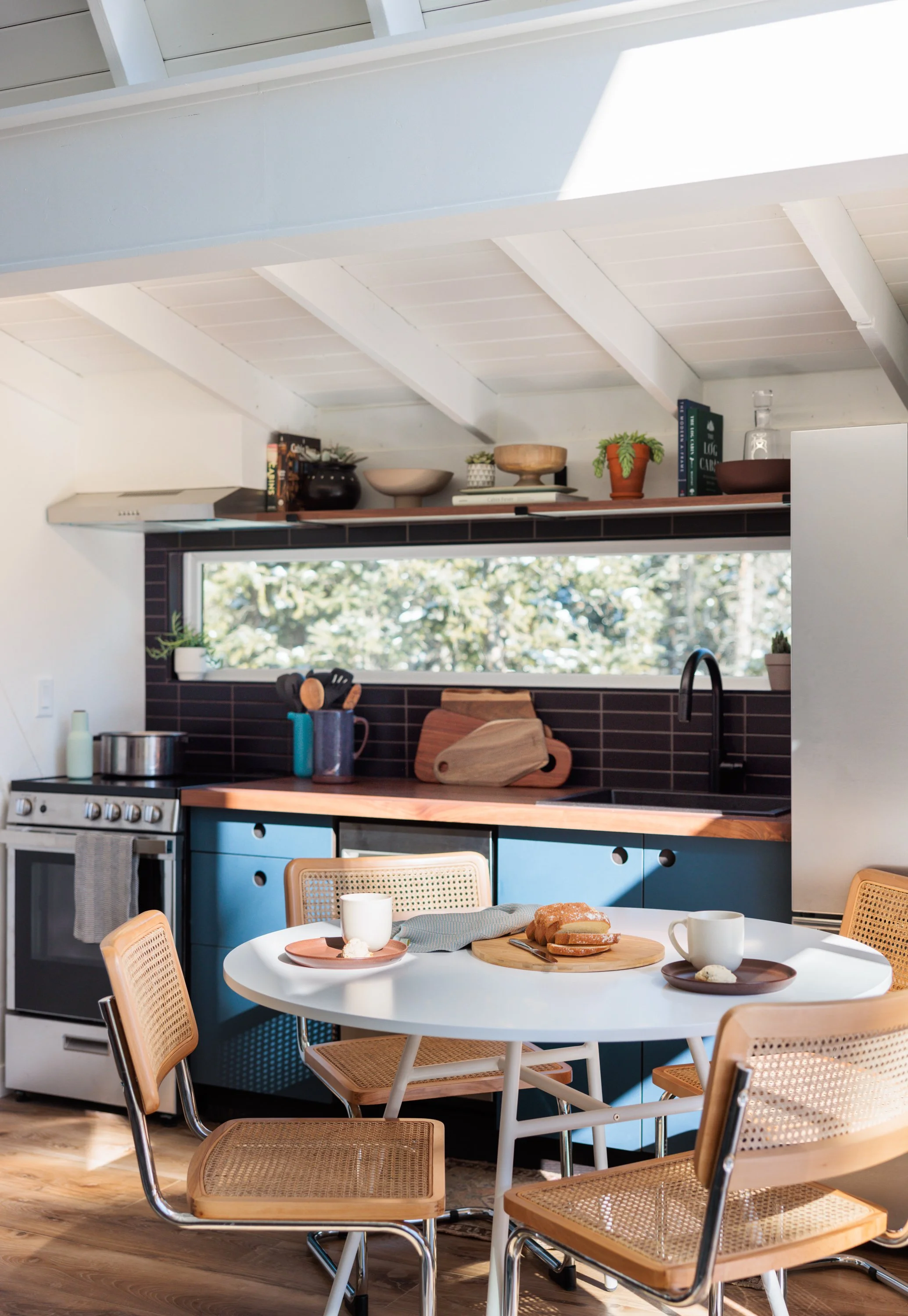 A-frame kitchen with blue cabinets, dark tile, and a round dining table.