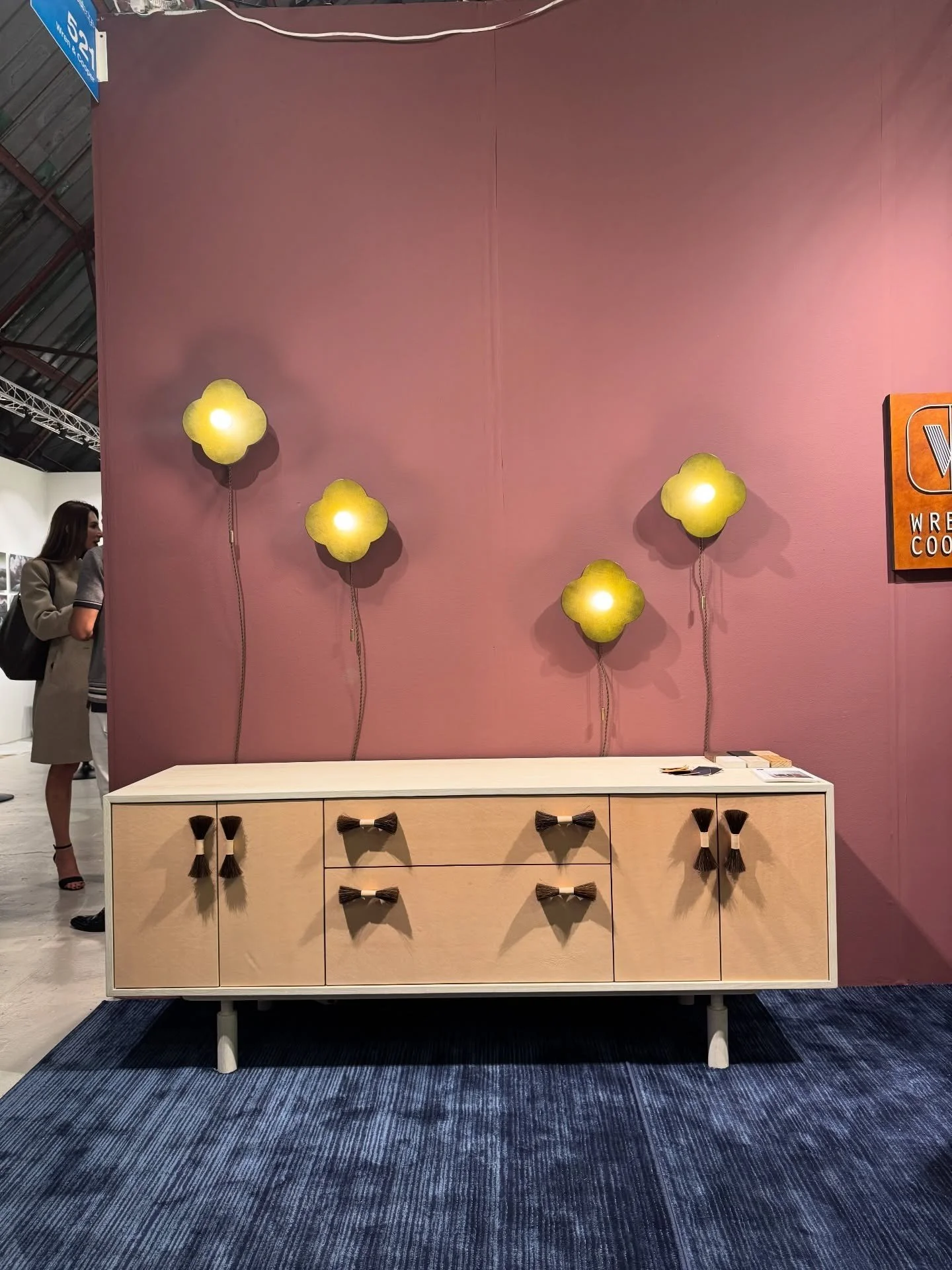Wood sideboard beneath yellow wall sconces on a pink wall