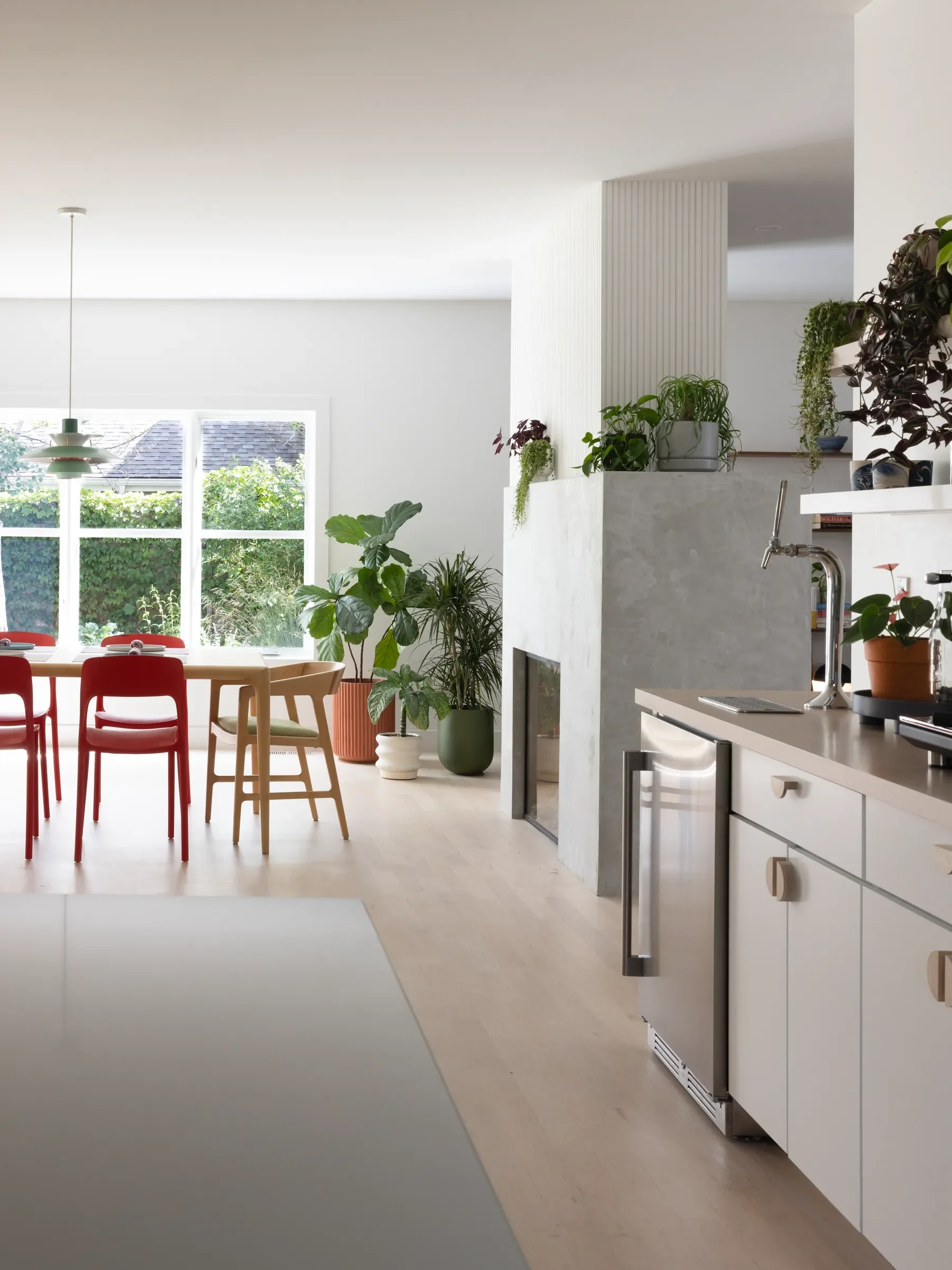Bright kitchen and dining area with white cabinetry, an island, red chairs, and plants.