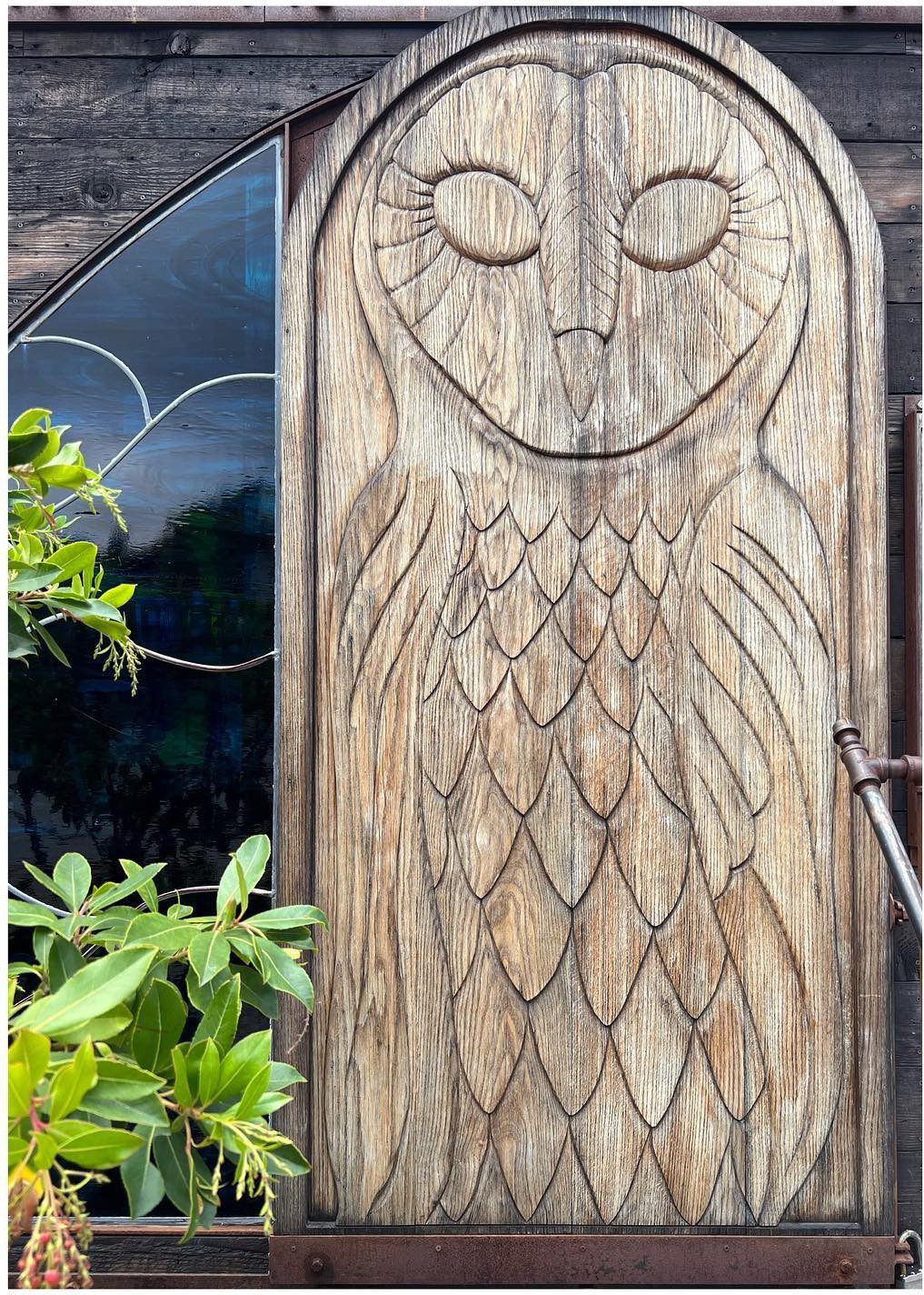 Tall carved wood door with an owl motif set in a dark exterior wall