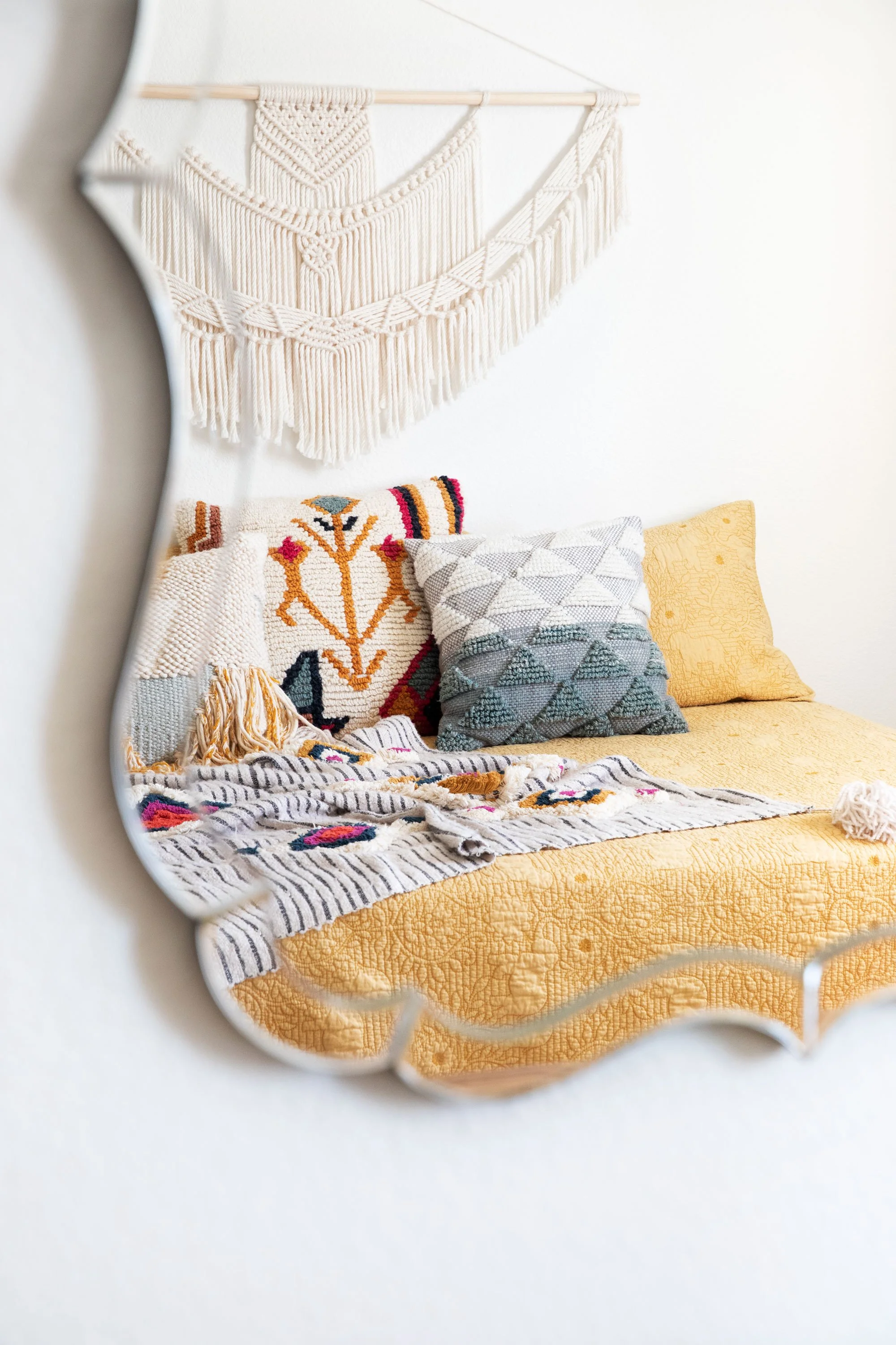 Textile wall hanging above a bed with layered patterned pillows and blankets.