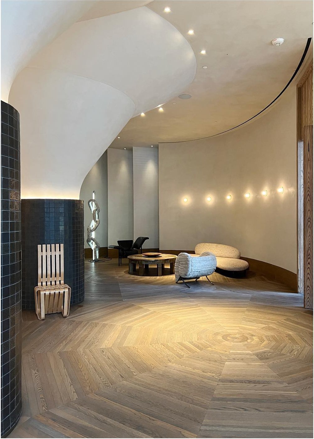 Sweeping curved wall and circular ceiling light above pale wood flooring