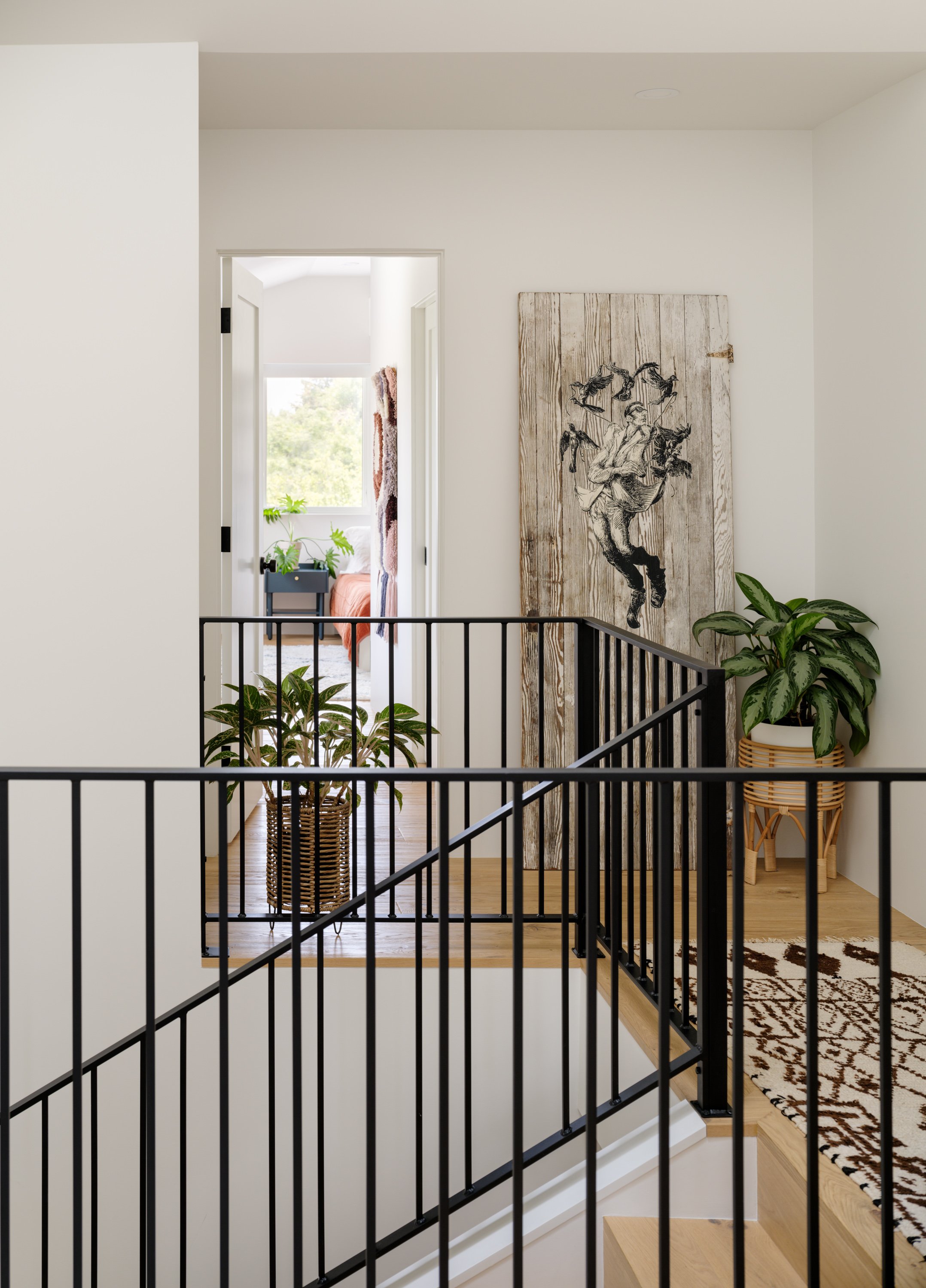 Bright stair landing with black railing, plants, and framed artwork.