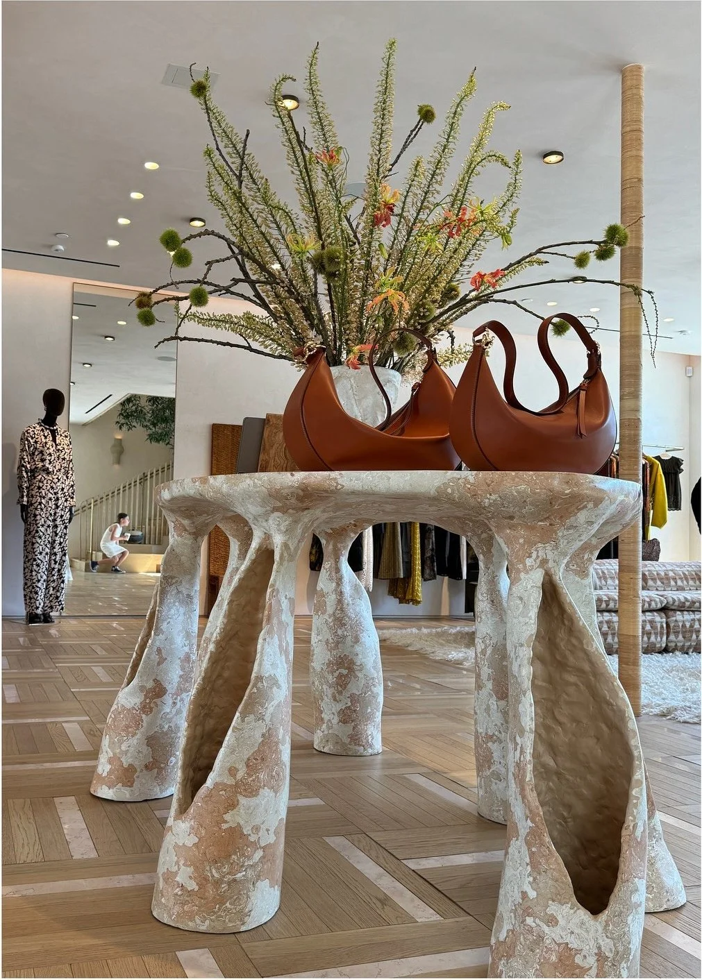 Sculptural stone display table holding leather handbags and a vase