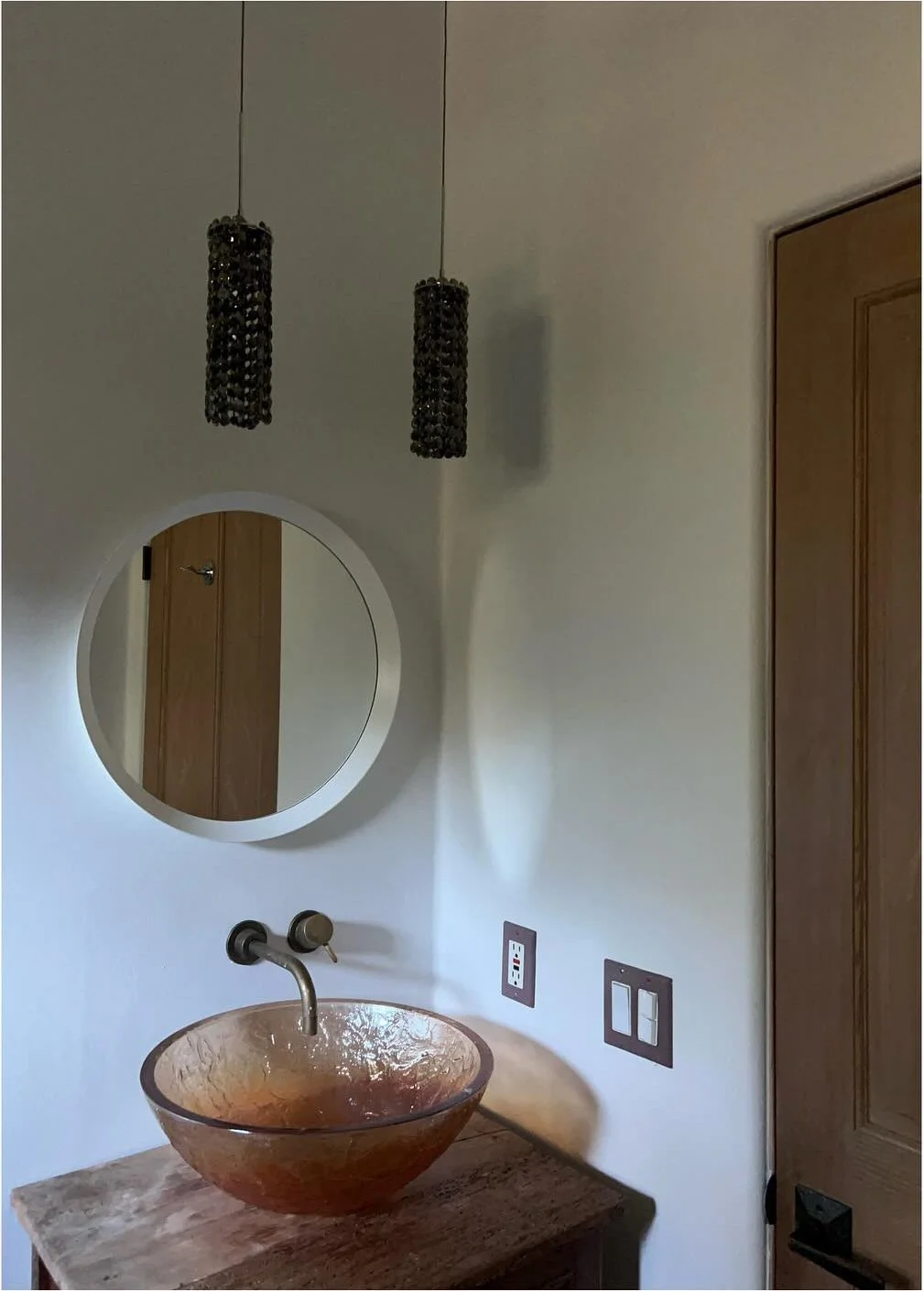 Glass vessel sink on a wood vanity beneath a round wall mirror