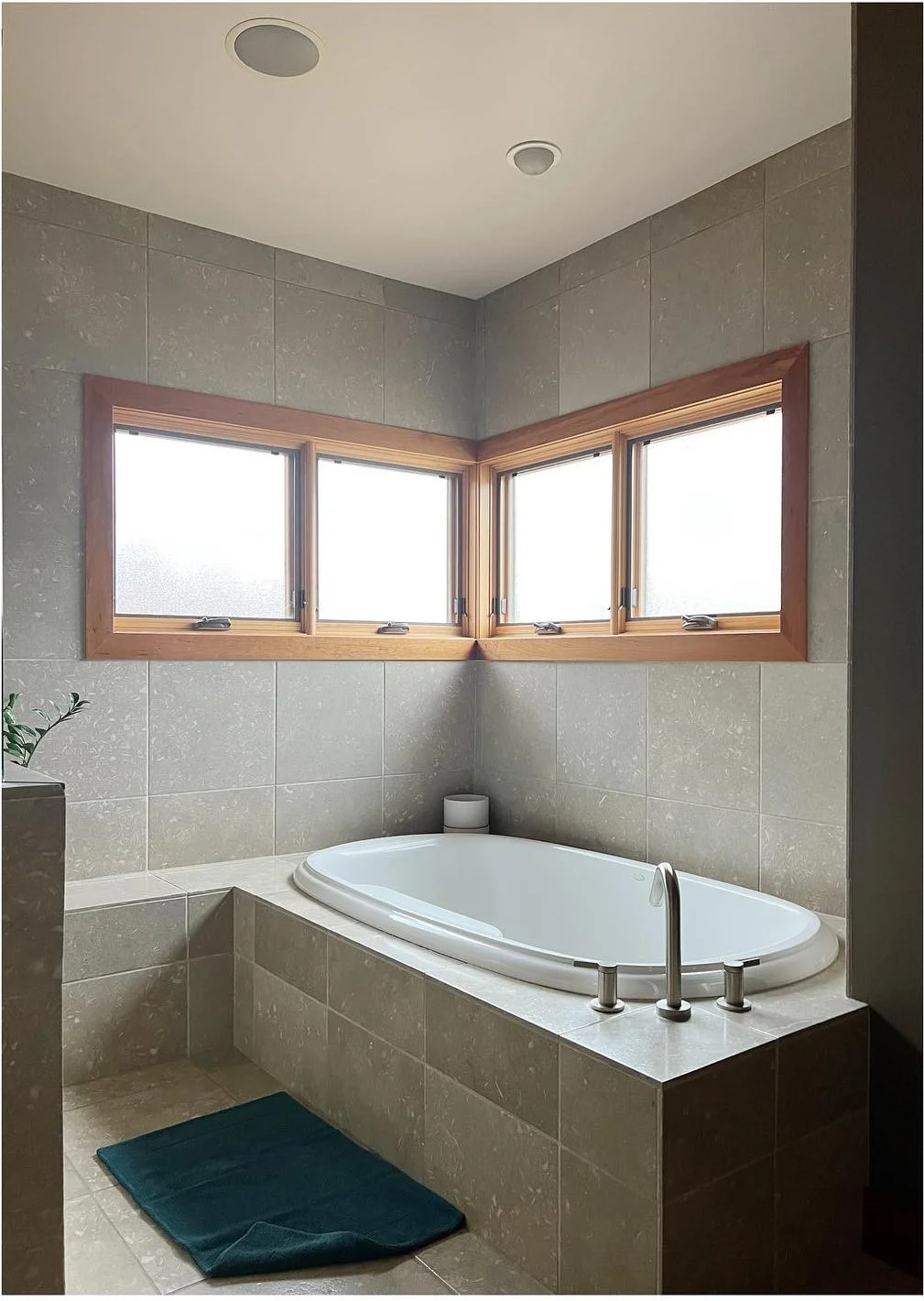 Original built-in bathtub surrounded by beige tile below corner windows