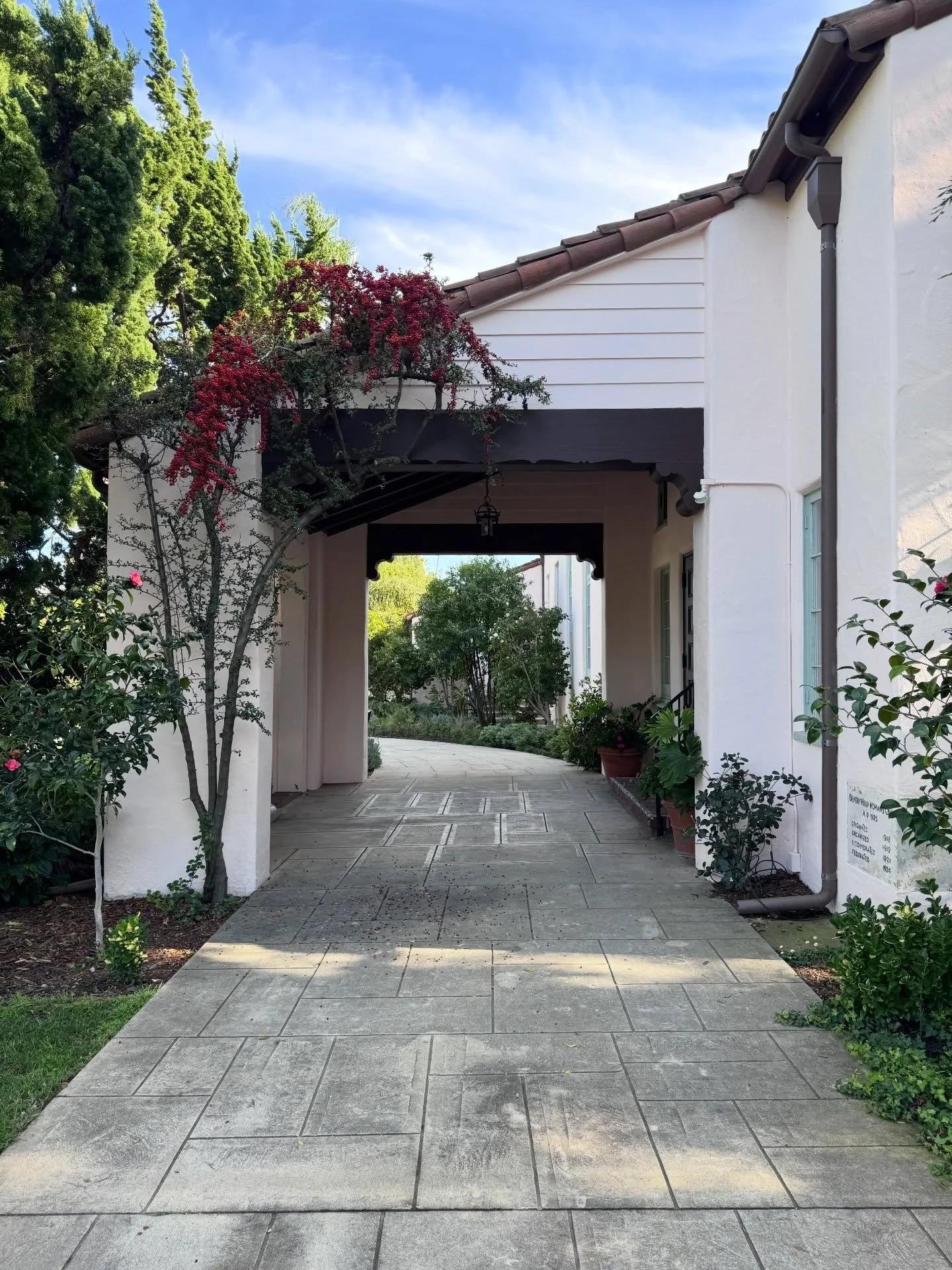 Paved walkway beside a white historic building and flowering vine
