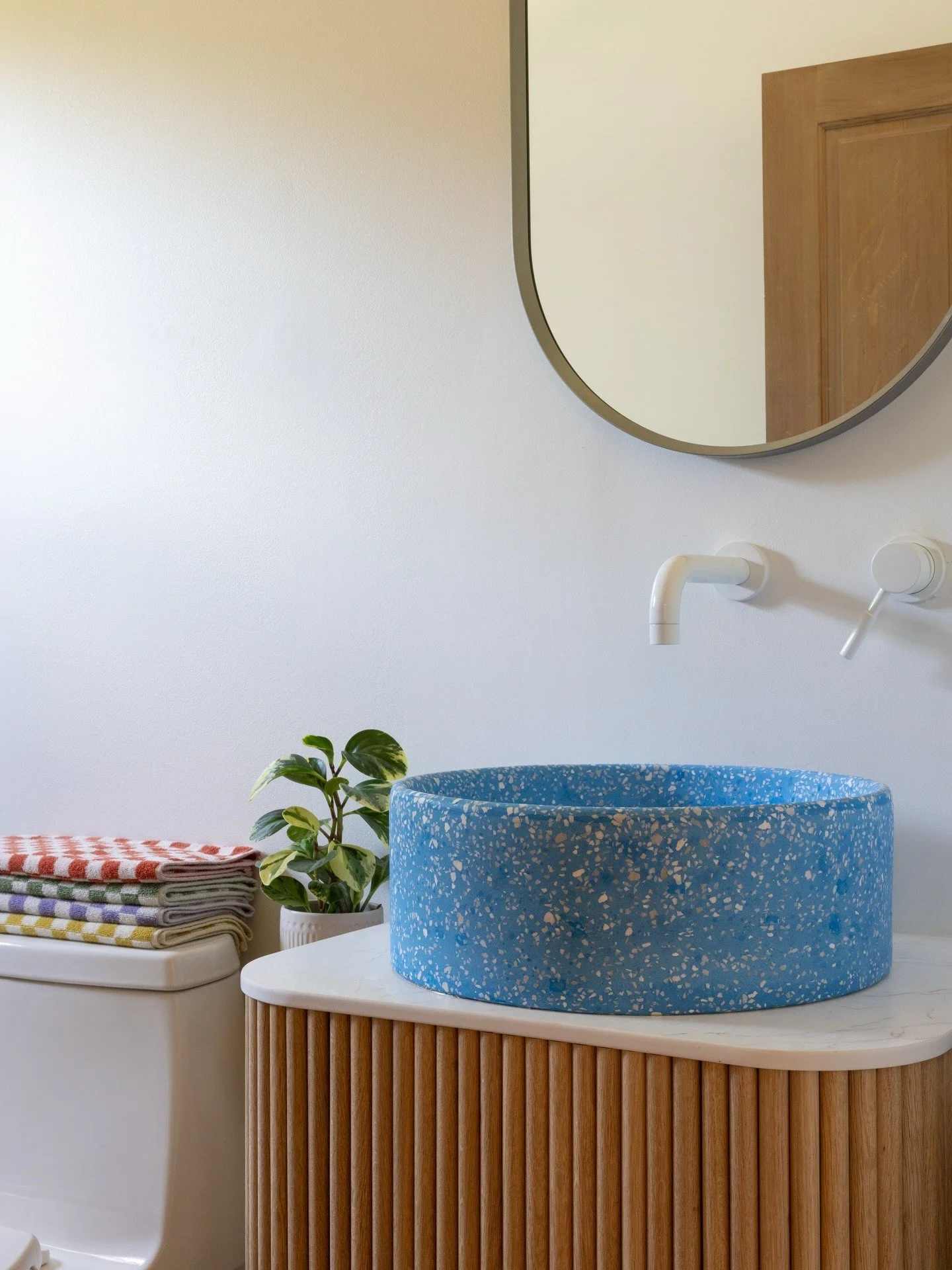 Blue terrazzo vessel sink beneath a wall-mounted white faucet