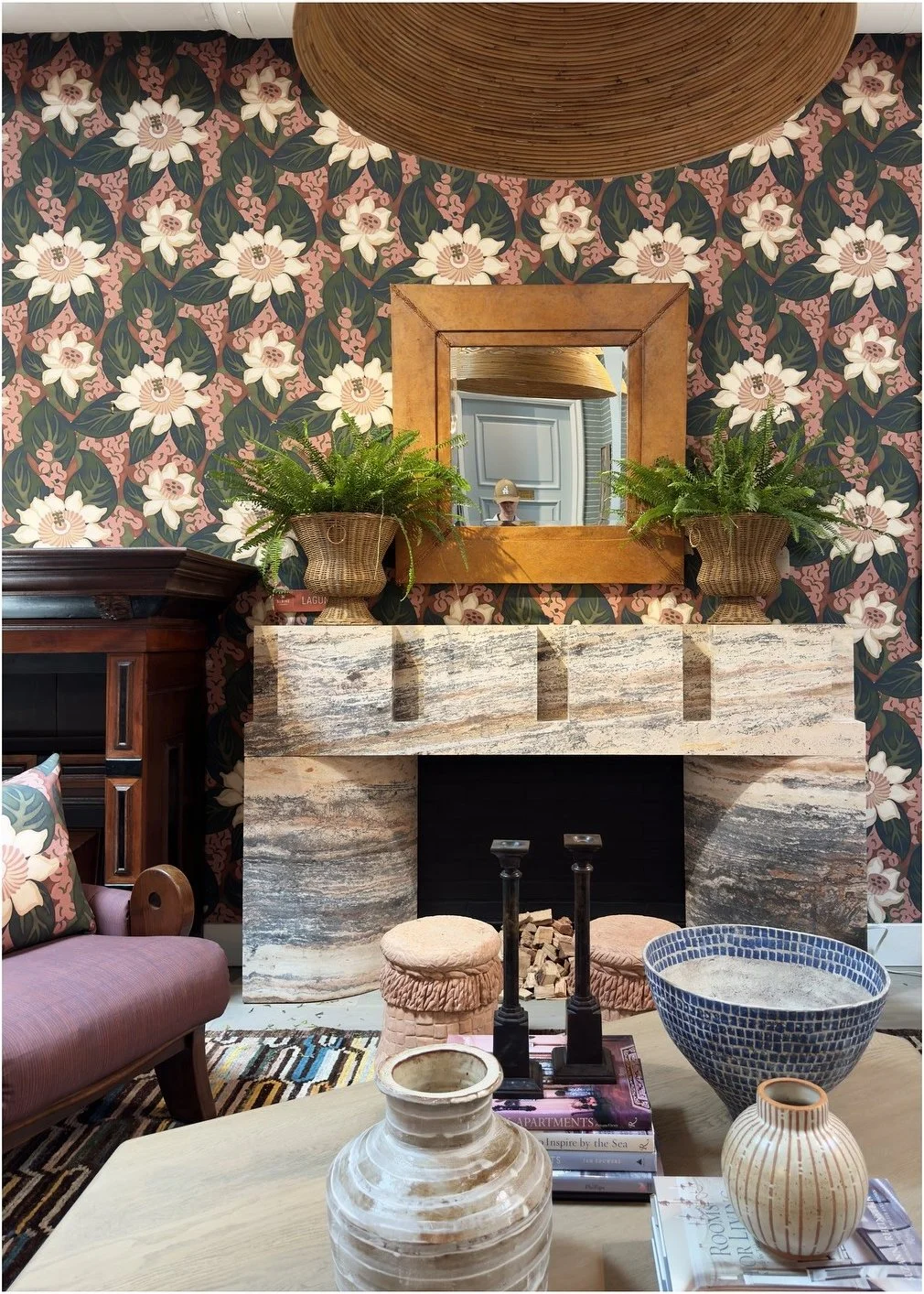 Floral wallpaper behind a stone fireplace and collected ceramics