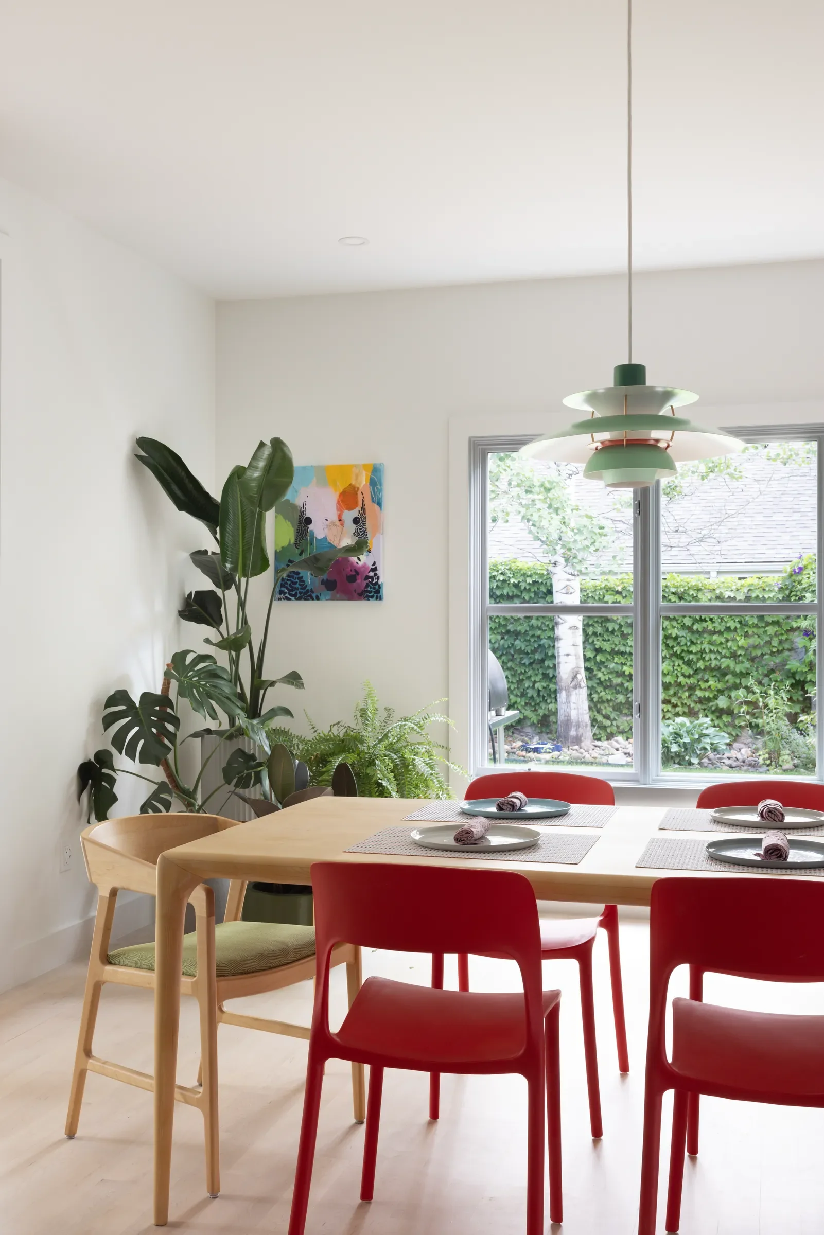 Dining table with red chairs, a pendant light, and plants by the window.