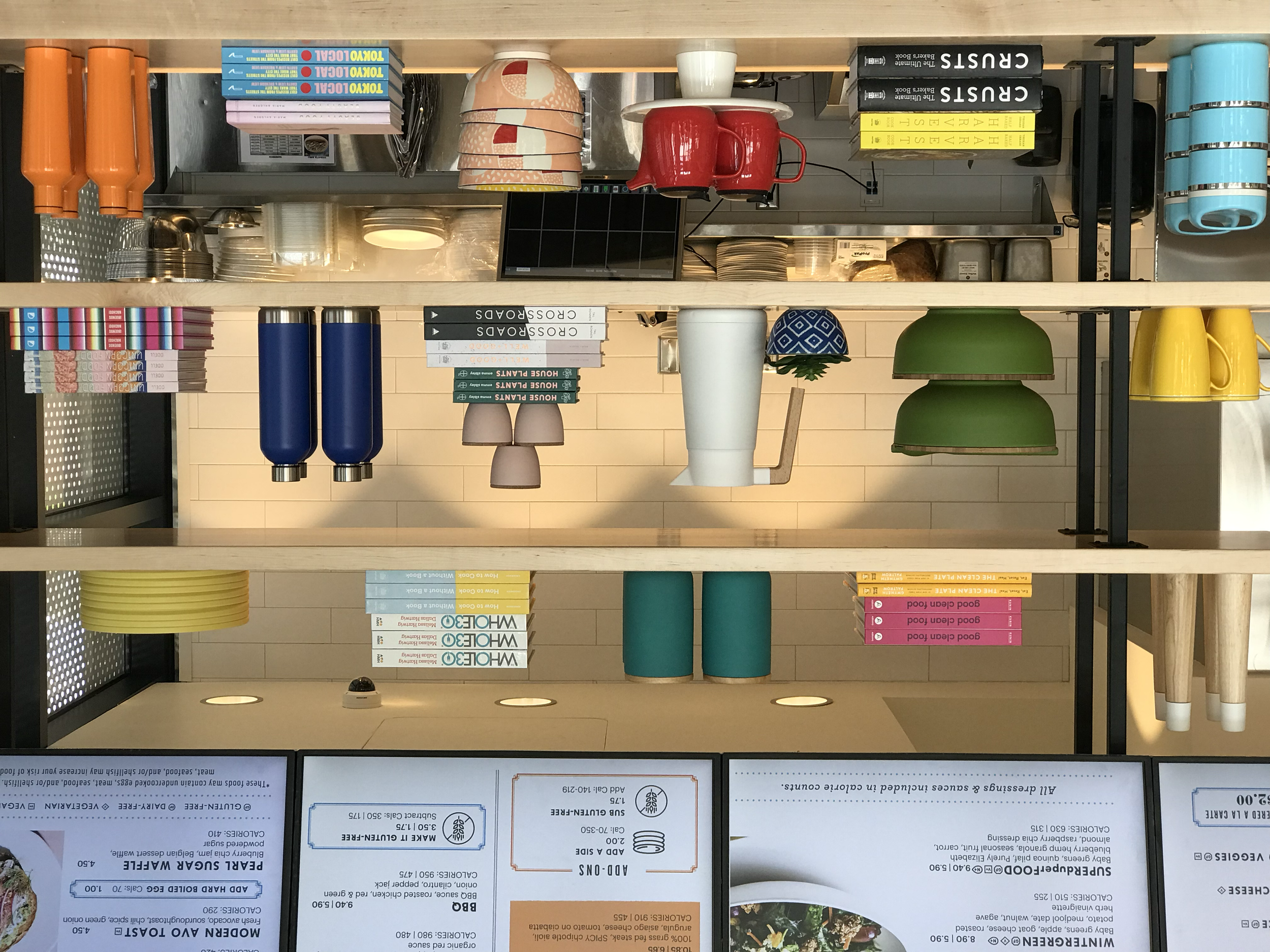 Restaurant shelving with colorful dishes, bottles, books, and menu boards above.